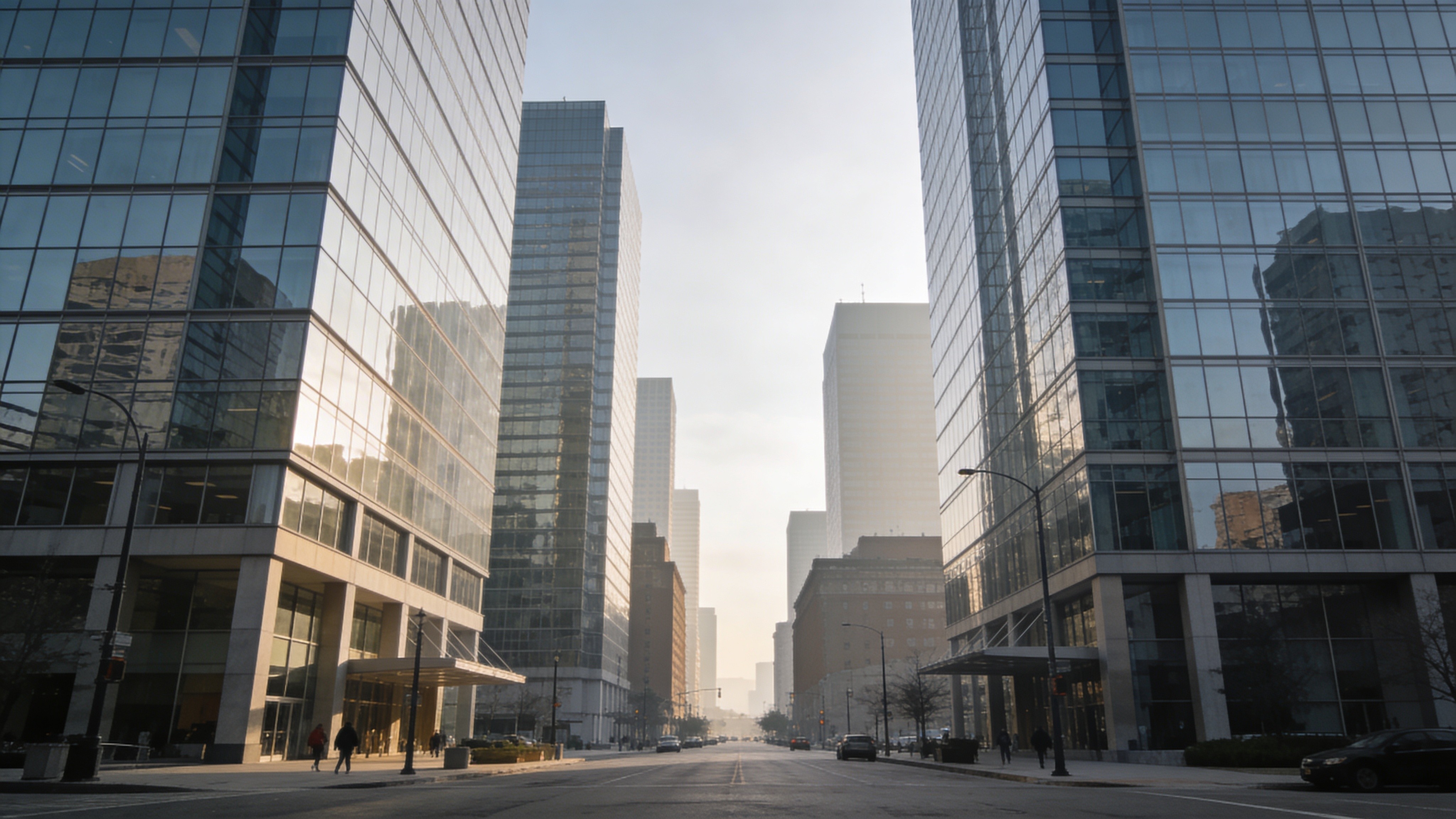 Wide city street flanked by modern glass office buildings during early morning with soft sunlight