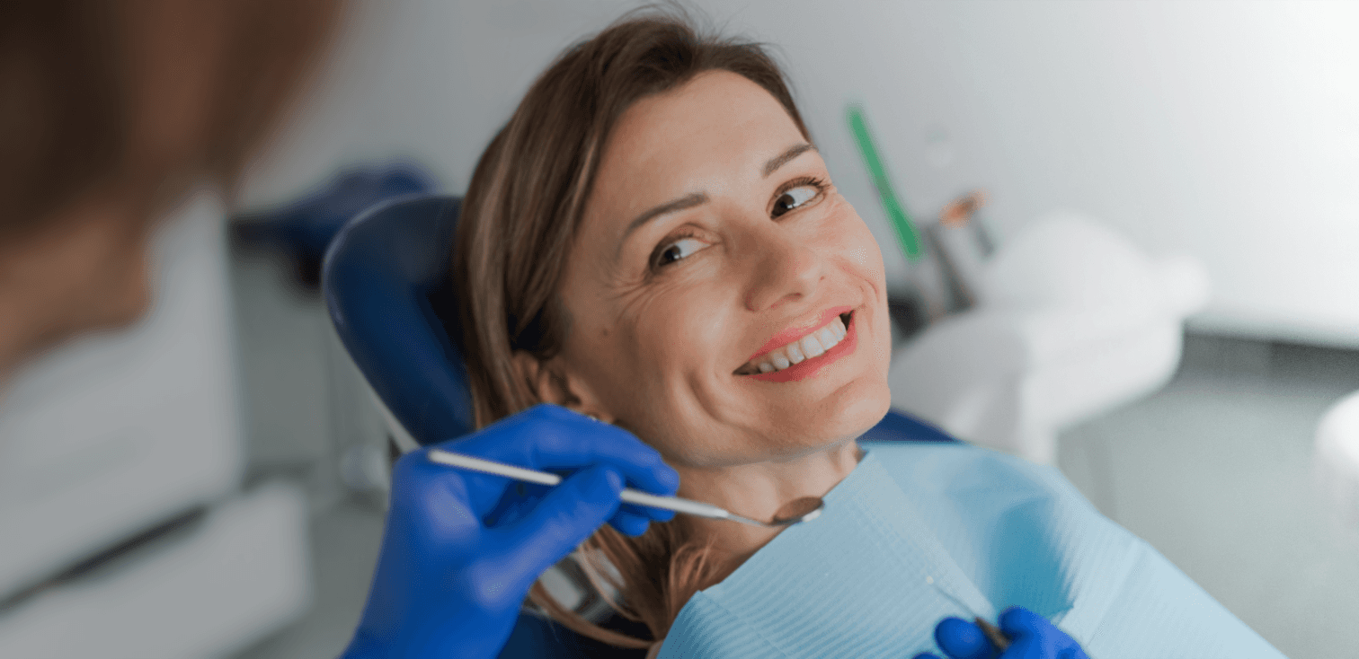 Kvinne smiler i tannlegestolen under en rutineundersøkelse hos tannlege.