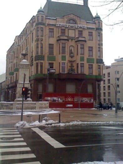 A photo of a multistore building with green roof and yellow walls that has a red banner with black and white photos on its front.