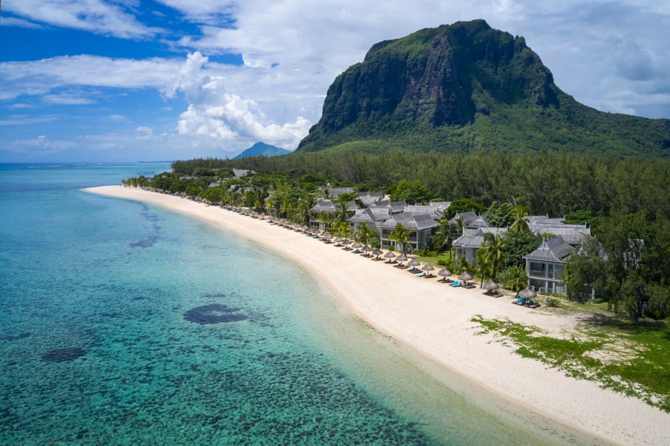 Luftaufnahme eines luxuriösen Resorts auf Mauritius an einem weißen Sandstrand mit kristallklarem, türkisfarbenem Wasser vor der Kulisse des Berges Le Morne Brabant.