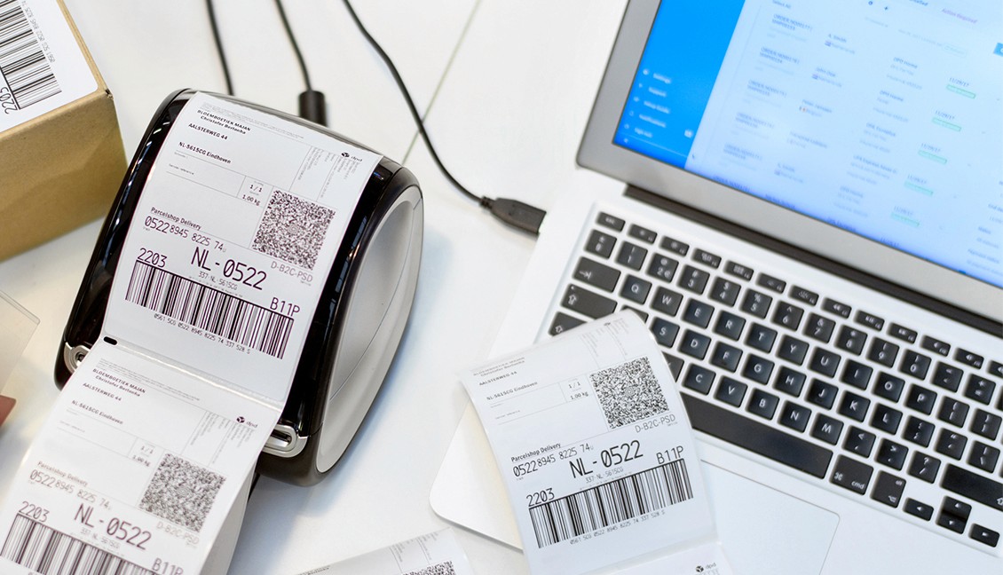 A label printer producing shipping labels next to a laptop