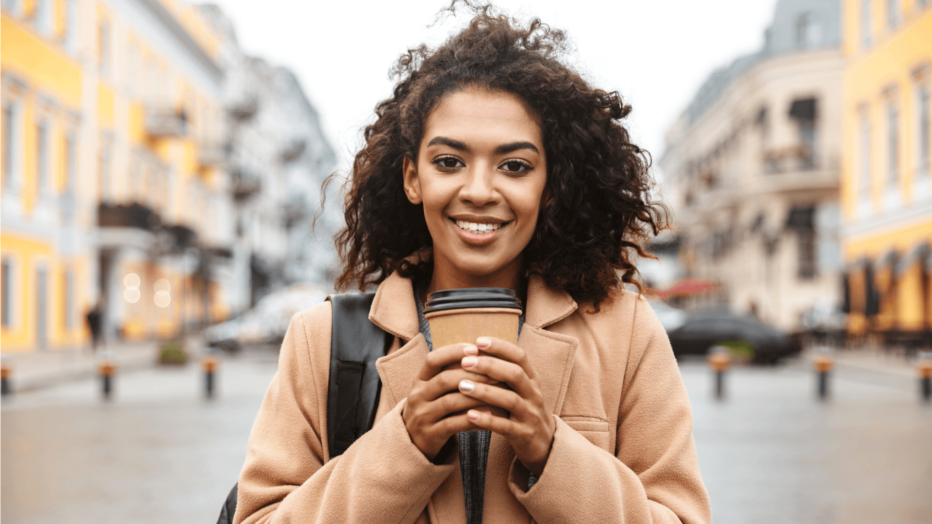 A smiling person holding a branded M&S takeaway coffee cup on a city street, demonstrating a user's positive interaction with the product in a real-world context.