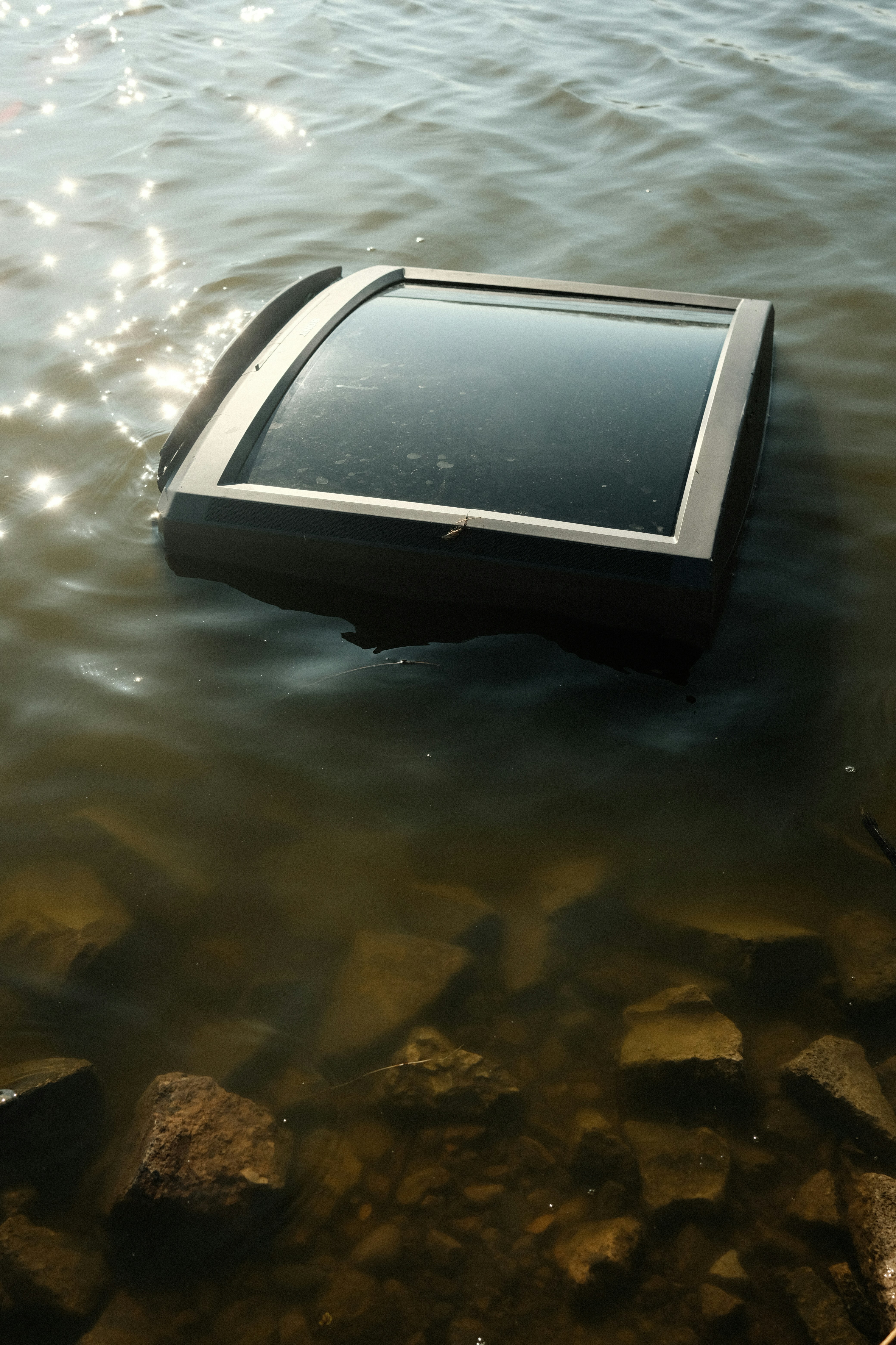 Television submerged in murky water near rocks