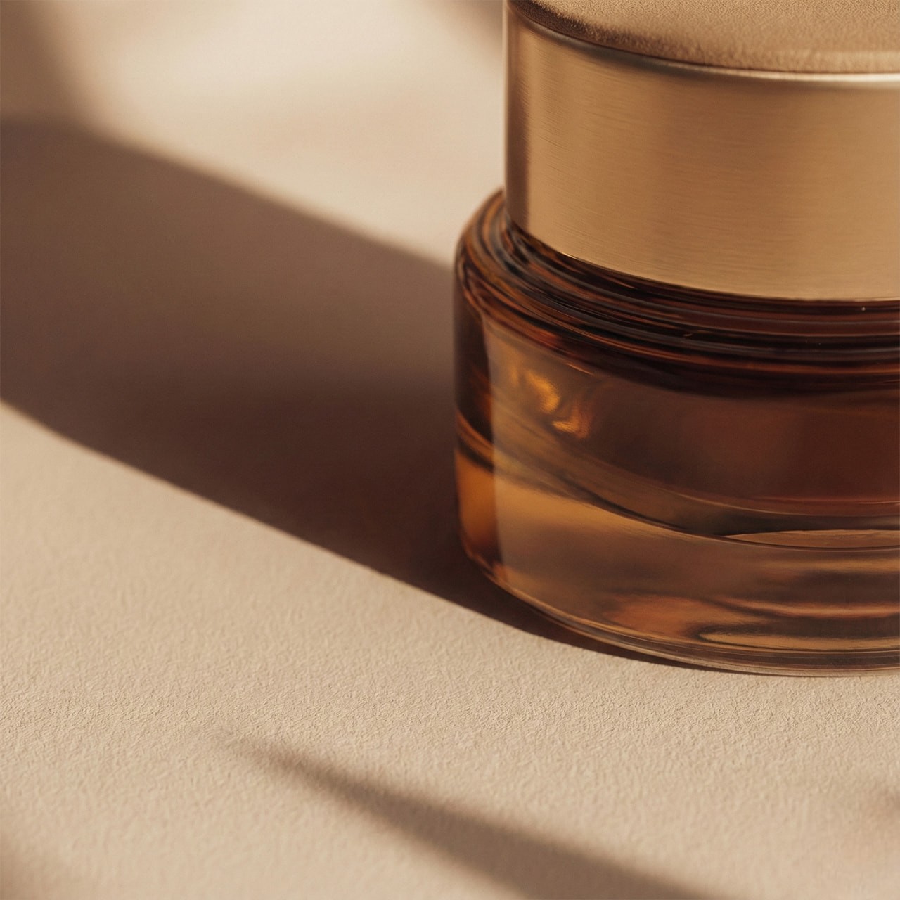 A glass jar with a metallic lid casts a soft shadow on a beige surface. Warm lighting highlights the subtle texture, creating an elegant, minimalist tone.