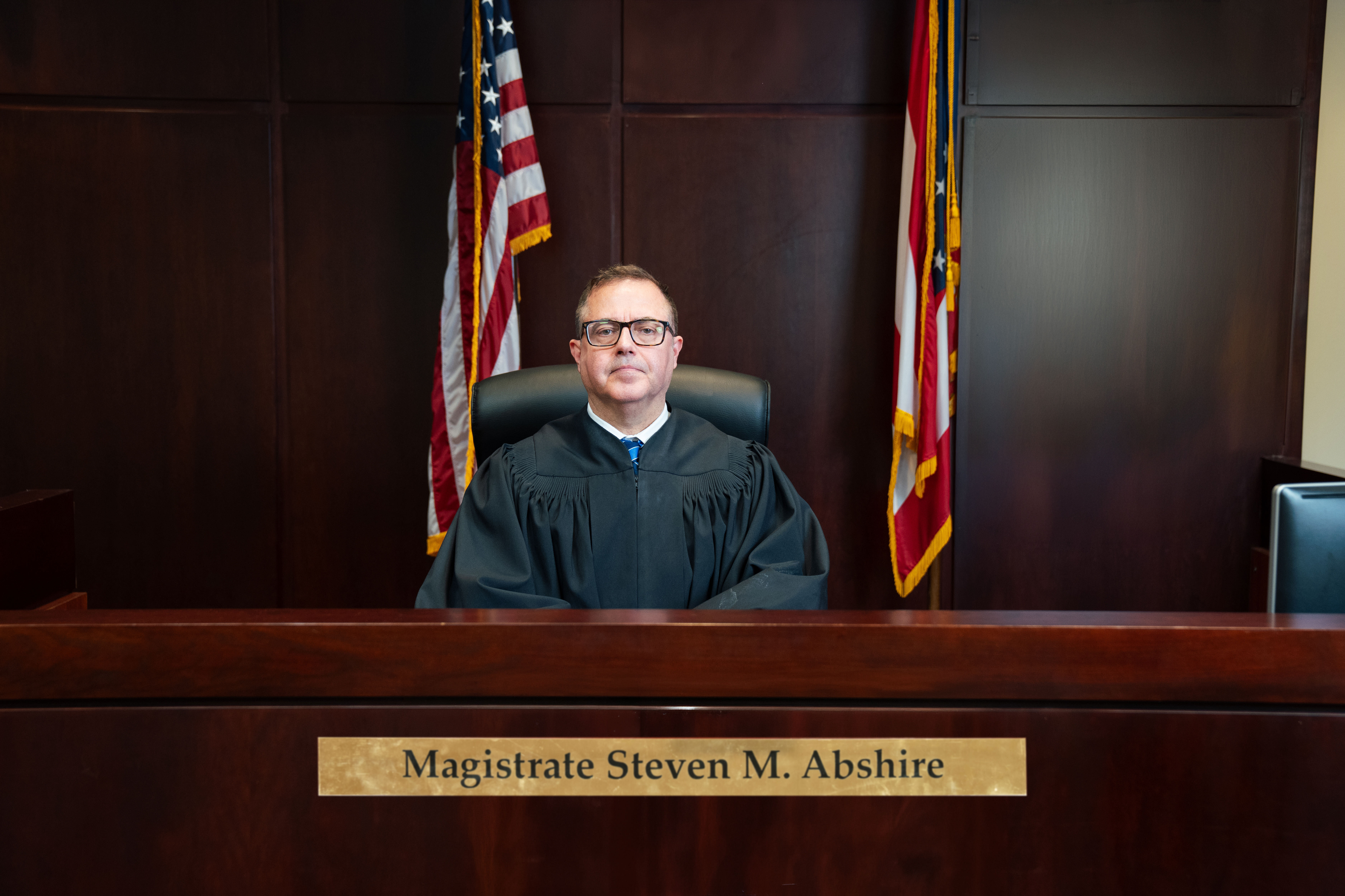Magistrate Steven M. Abshire seated on the bench in judicial robes beneath the Great Seal of Ohio