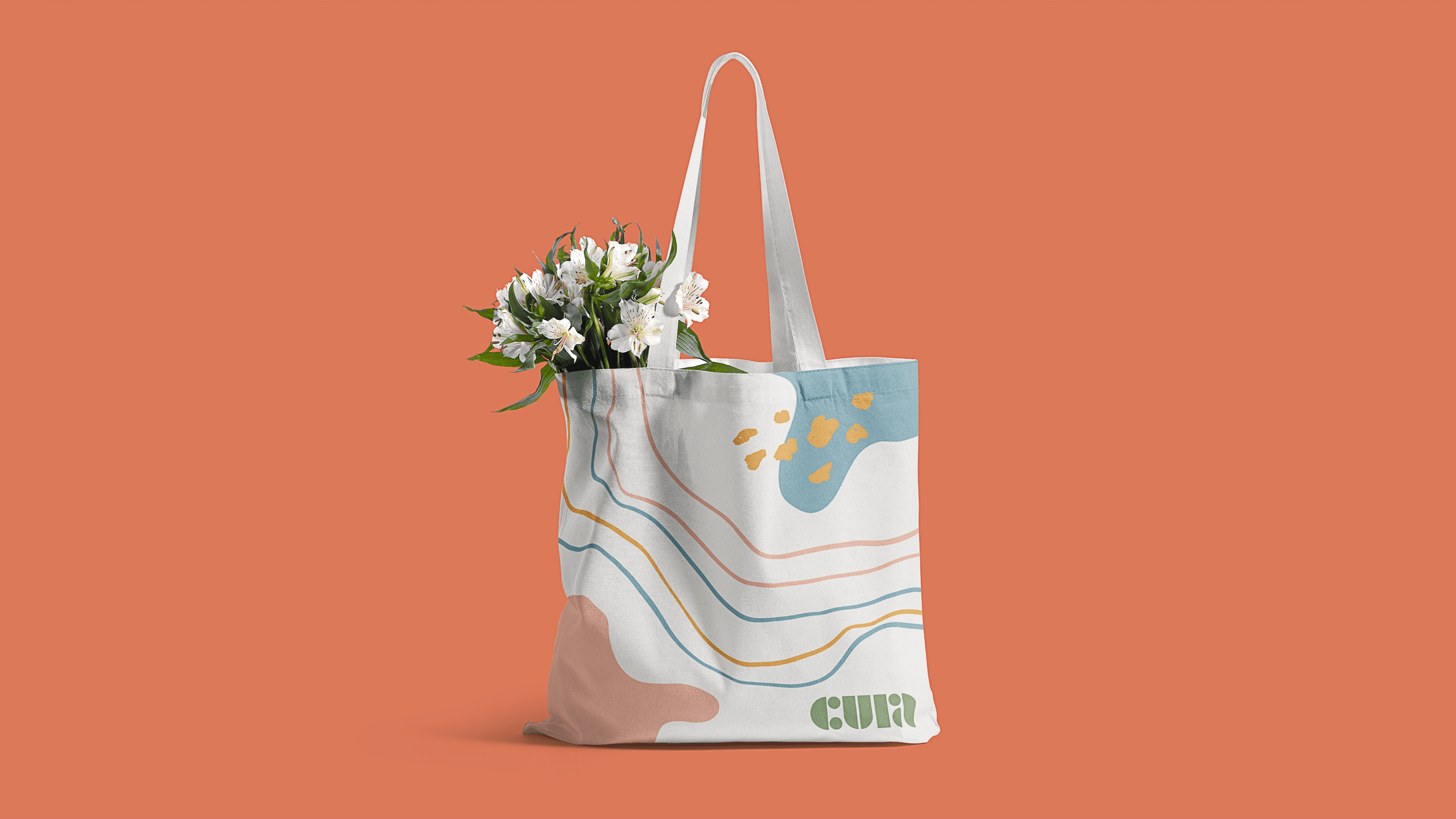 A white tote bag with blue and orange abstract designs sits against a solid orange background. The bag has two white straps and features the word "CULT" in a green font near the bottom. Inside the bag, white flowers with green leaves are visible.