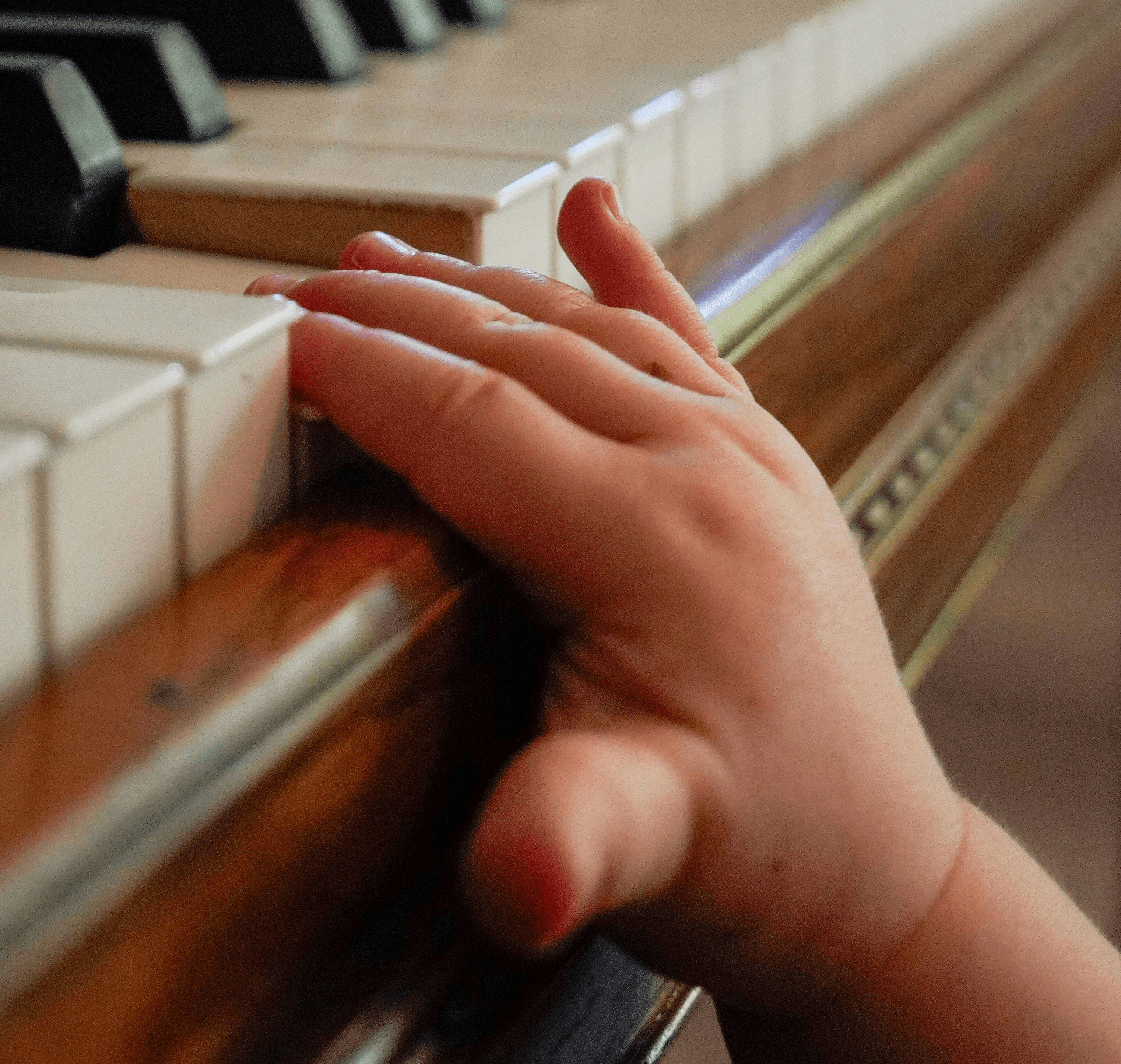 A child's hand rests on a piano keyboard.