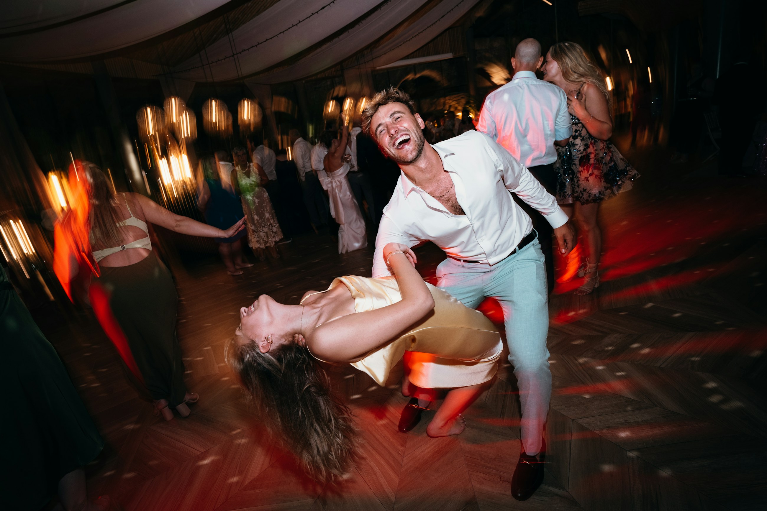 Couple dancing wildly at a wedding after party, blurred by motion and red light