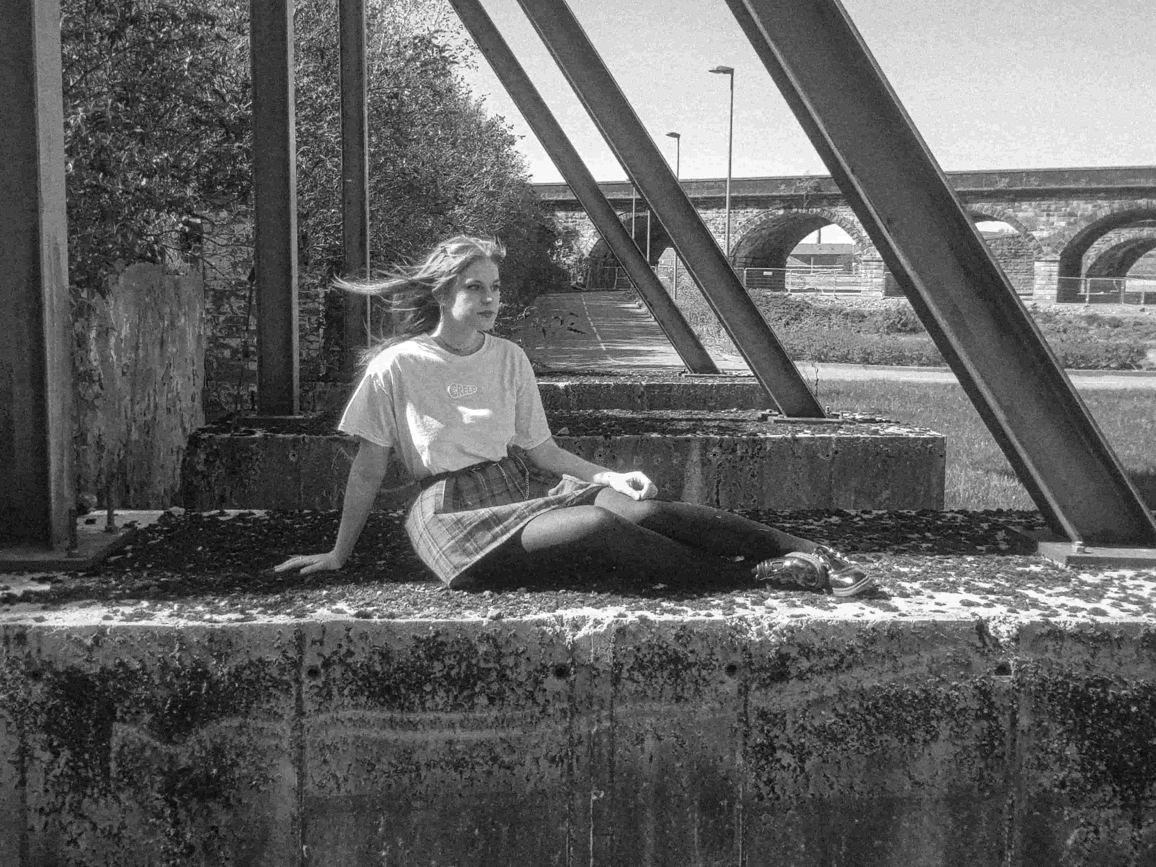 Photograph of streetwear model sat on concrete  - photo has a black & white filter.