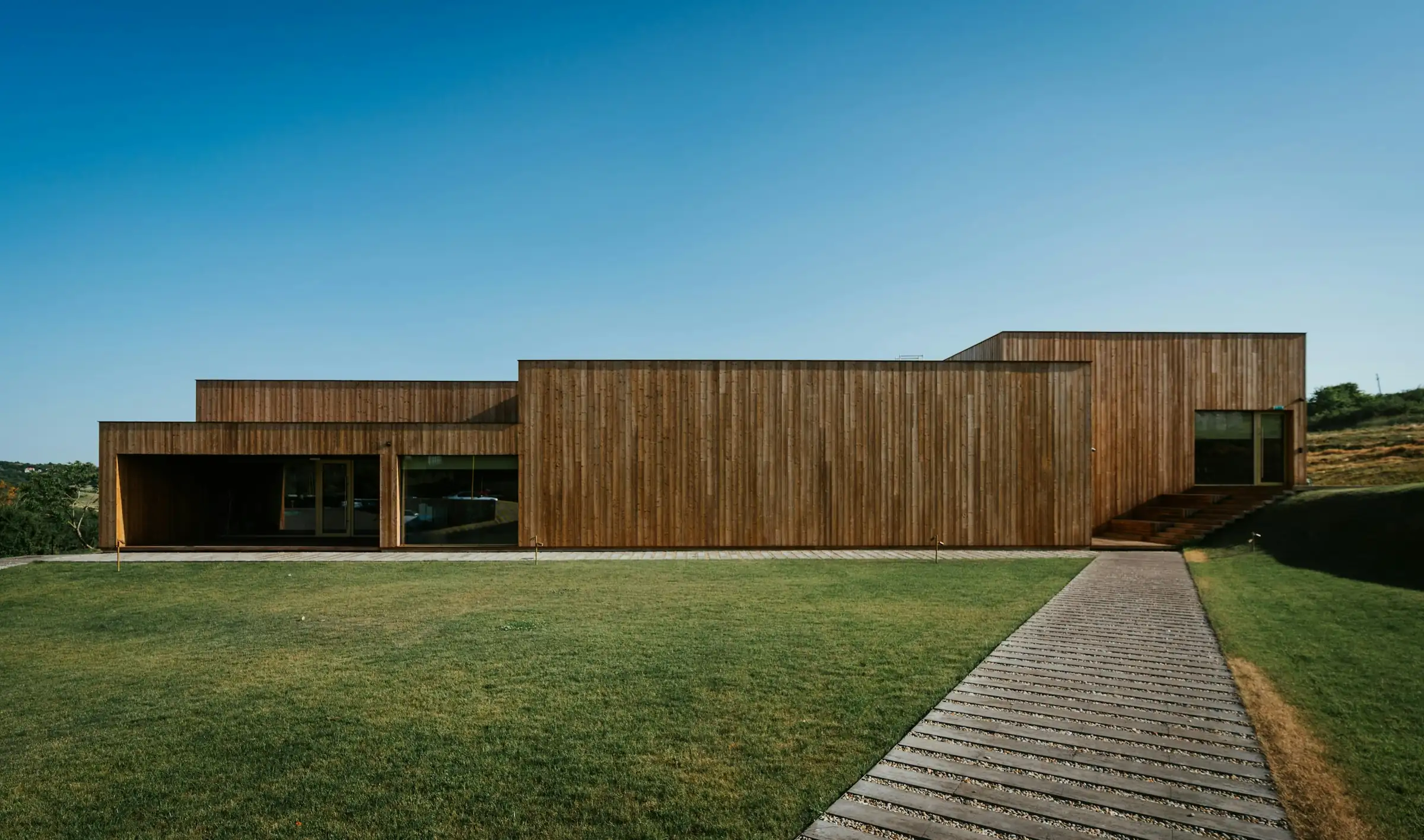 Modern timber-clad residence with horizontal wood facade and geometric volumes set on manicured lawn