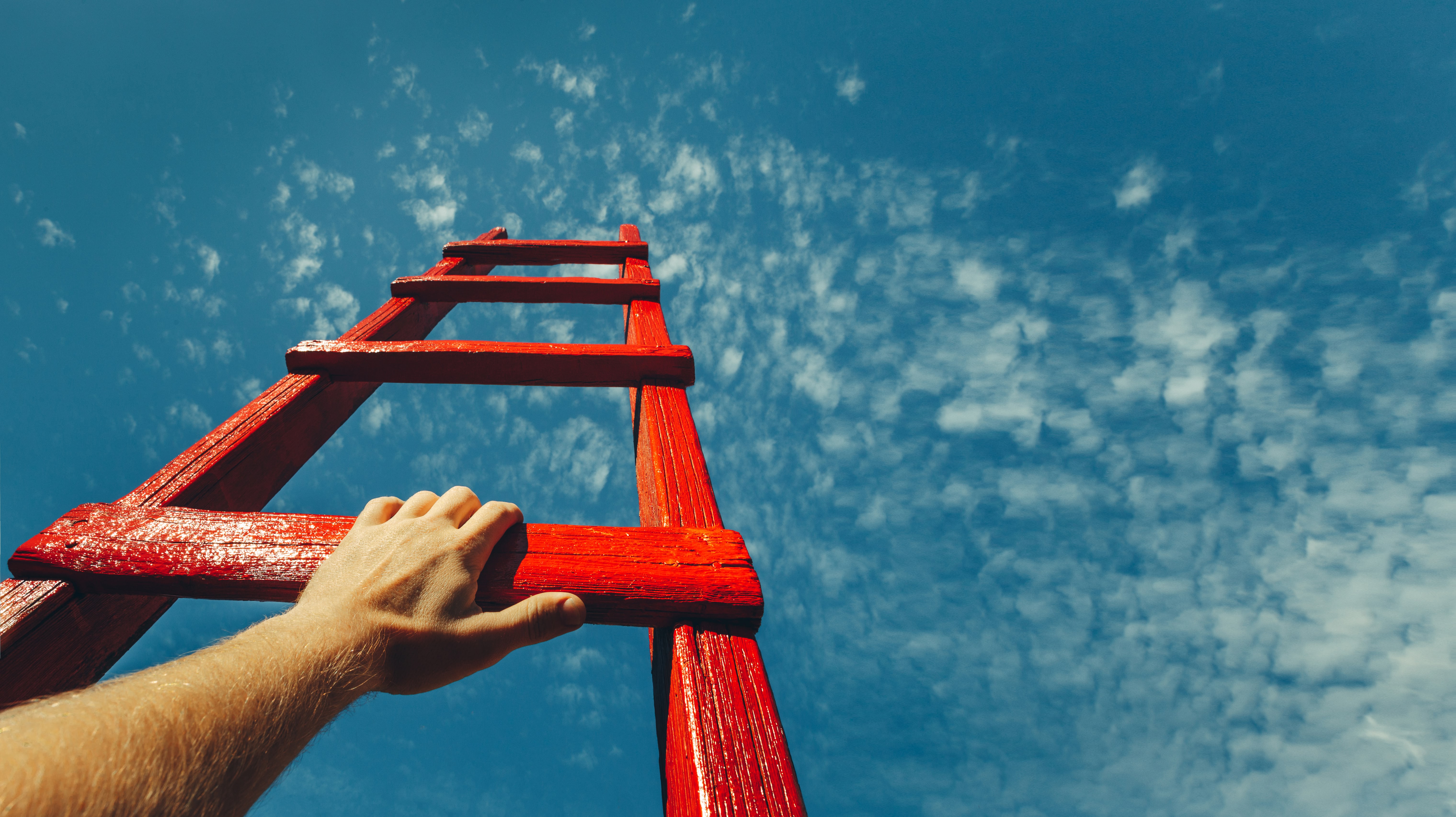 Une personne grimpant sur une échelle rouge sous un ciel bleu.