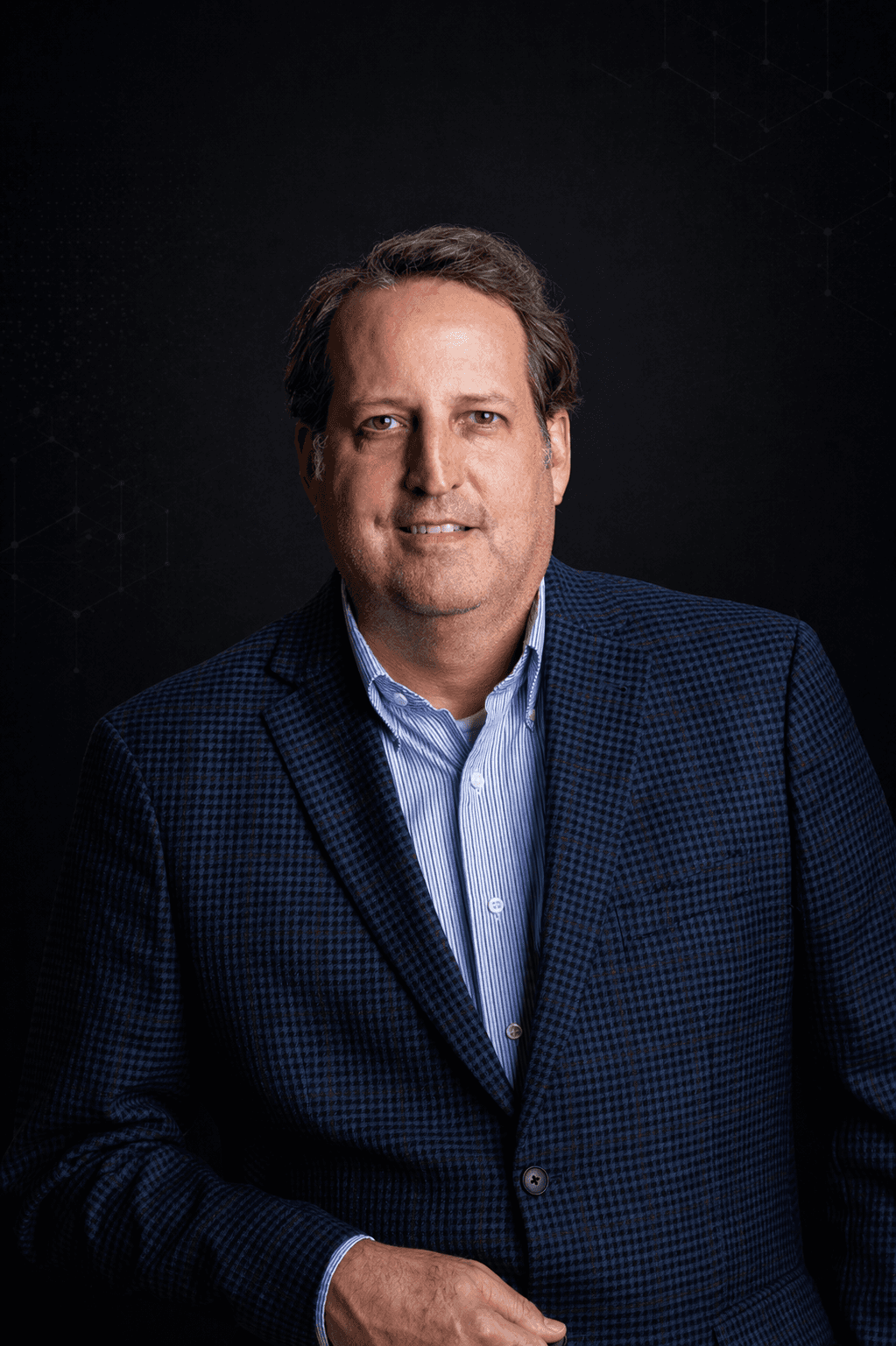 Professional portrait of a man in a blue check blazer against a dark, softly lit technology-inspired background, conveying executive leadership, enterprise credibility, and alignment with DistroLogic’s modern governed-execution brand.