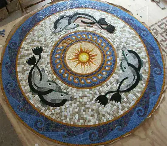 Circular mosaic medallion with four dolphins around a sun and a wave scroll border, laid out in the studio.