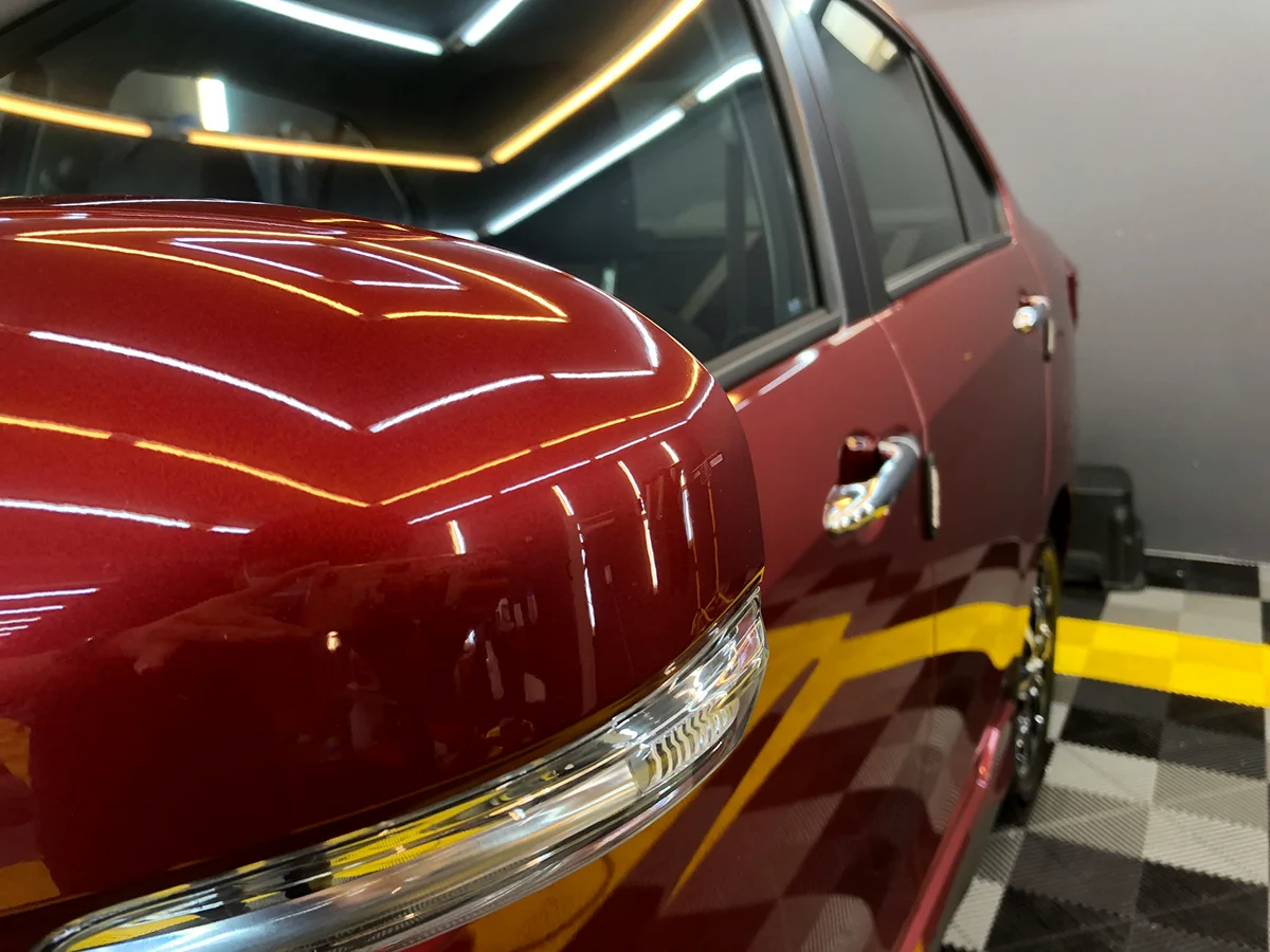 Red luxury car with high-gloss paint and ceramic coating protection under showroom lighting.