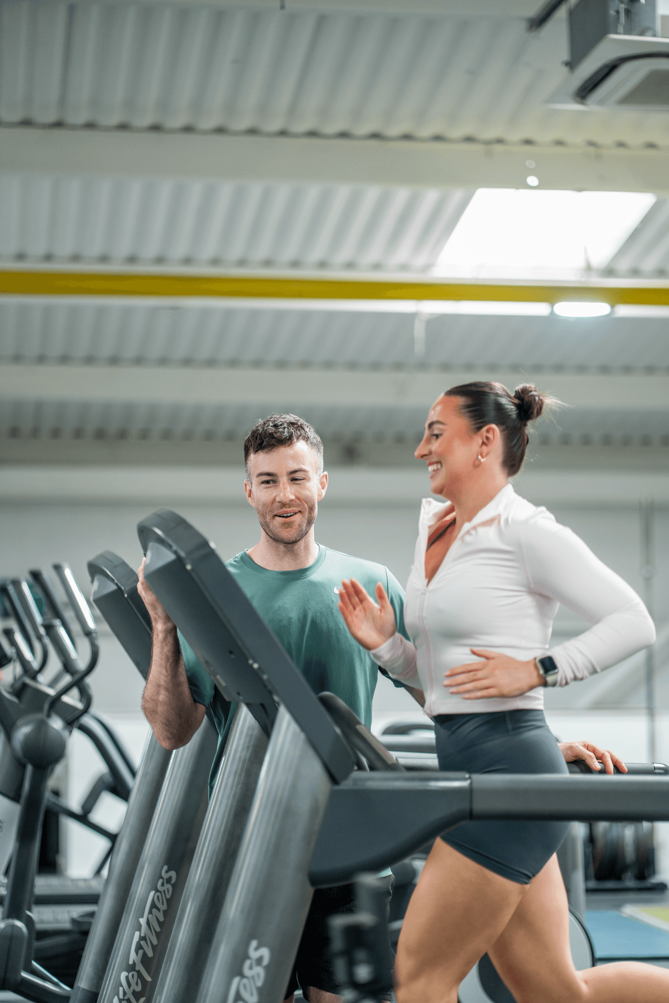 Woman running on treadmill and smiling with a personal trainer stood next to her