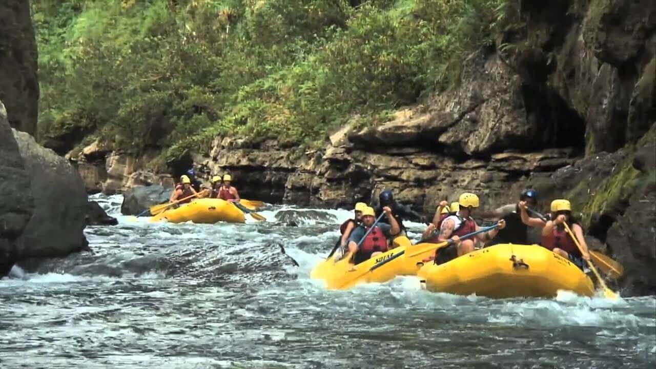 A group in yellow rafts navigates river rapids through a narrow, lush gorge. A Fiji adventure.