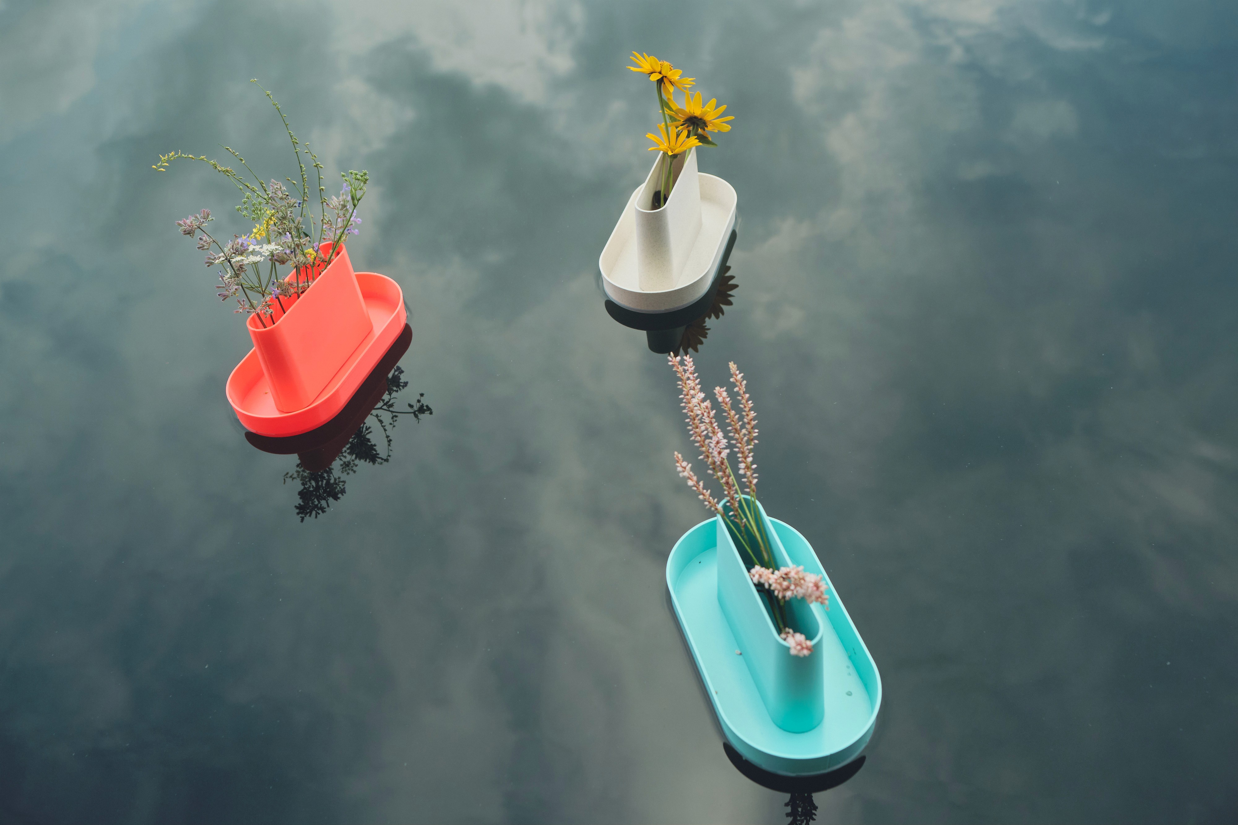 Three small organizers in red, green, and white float on calm water, reflecting their colors on the surface.
