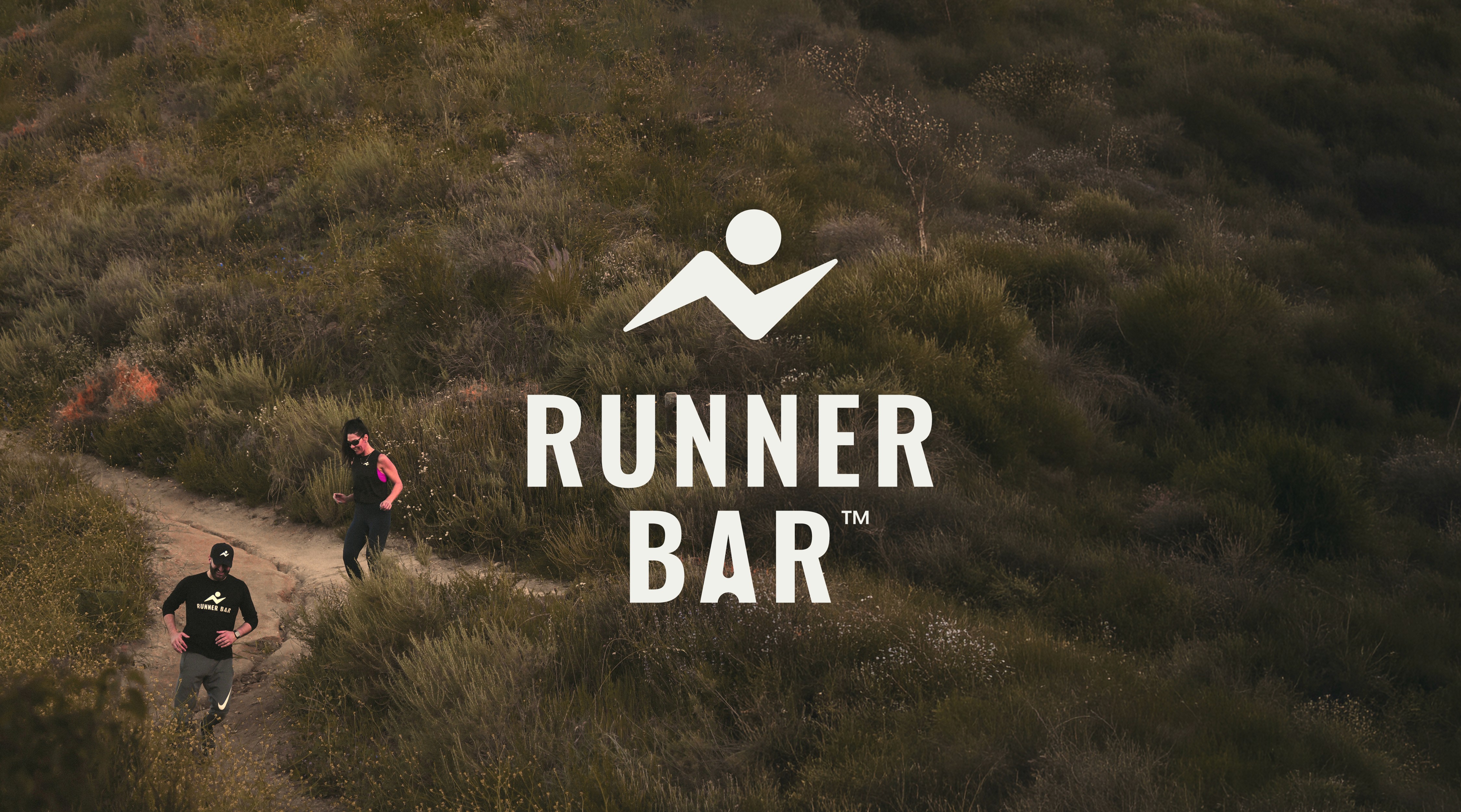Runner Bar logo overlaid on an aerial shot of two people trail running on a hillside.