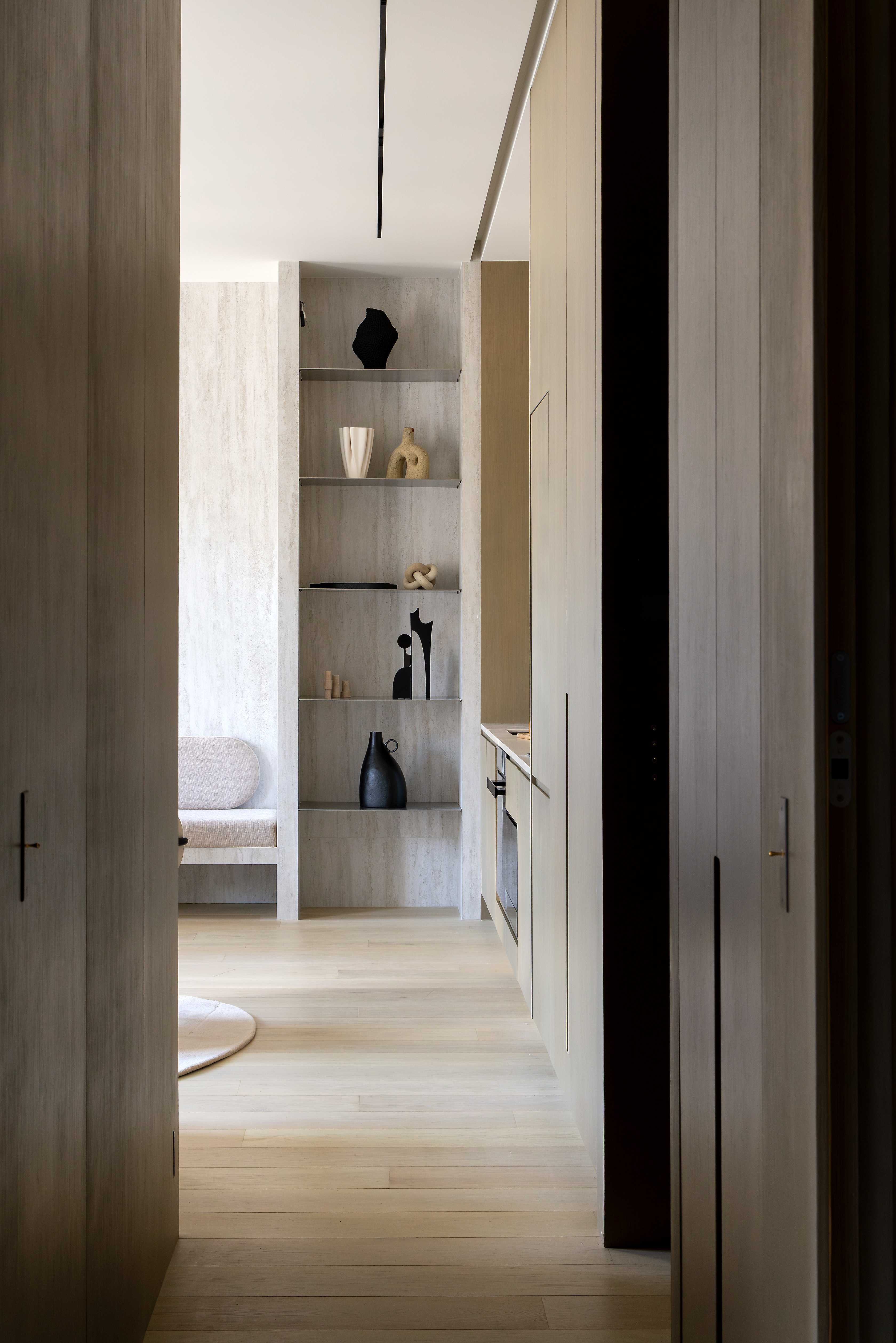 Perspective depuis le couloir vers le salon avec bibliotheque decorative, objets d'art noirs et parquet clair