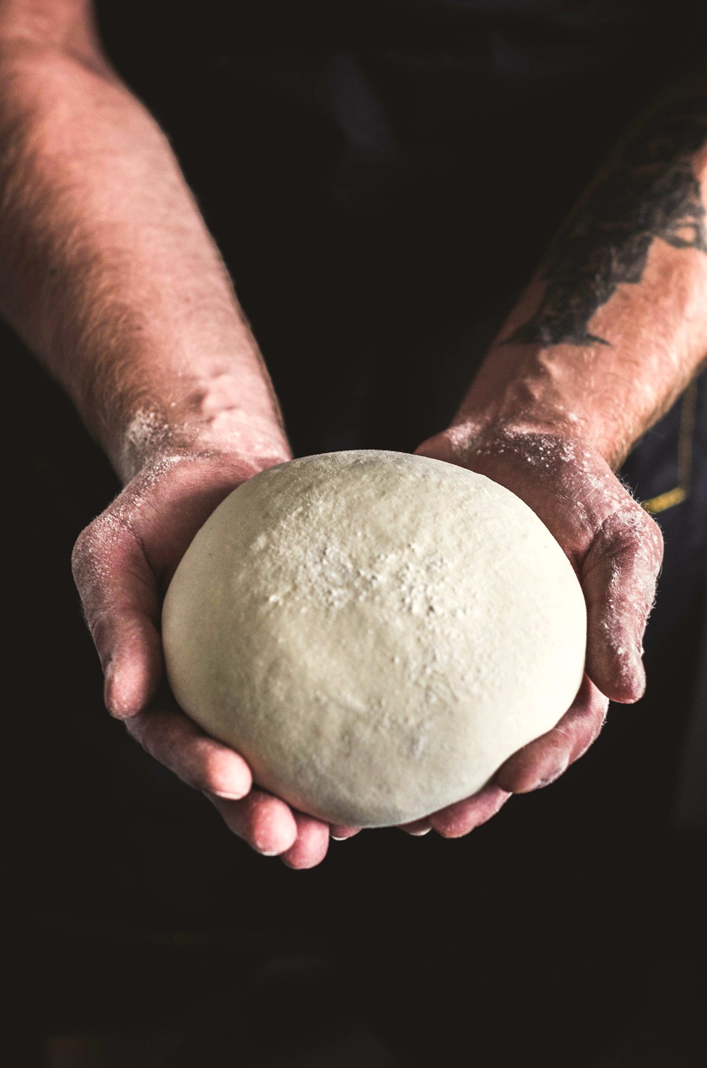 Hands holding a ball of rested dough