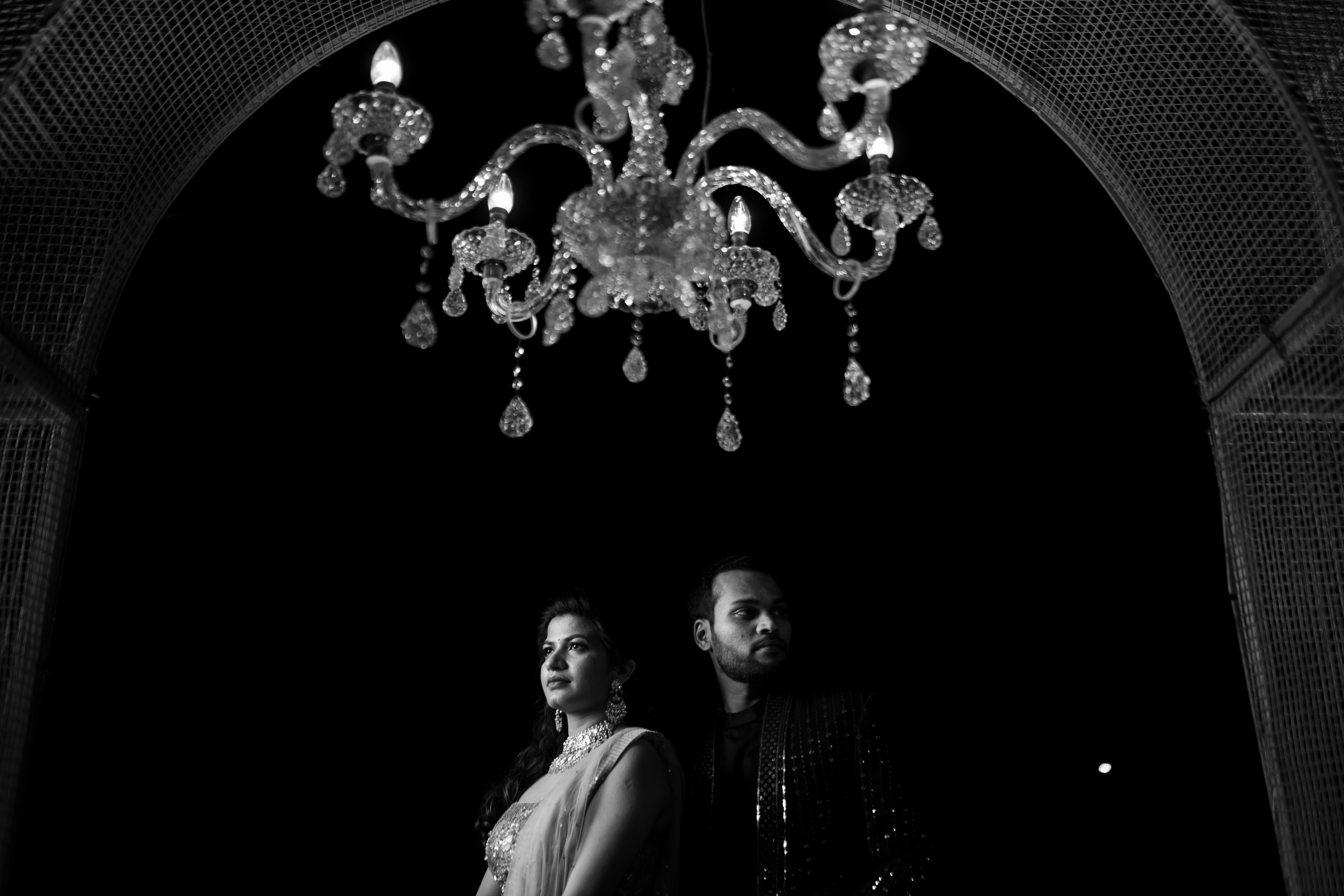 Mounika and Satya pose under a chandelier. Black & white Fine Art Wedding Photography in Hyderabad by Out of The Blues.