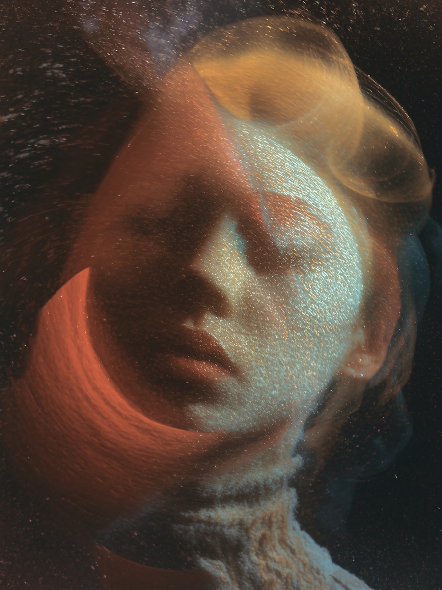 Artistic portrait of a woman with eyes closed, featuring a soft focus and an overlay of orange and yellow light.