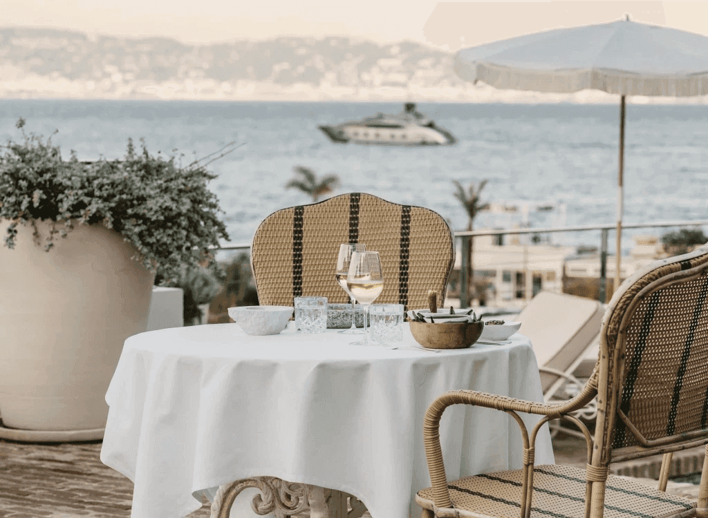 Elegant seaside terrace set with wine glasses and sunlit rattan chairs, evoking relaxed luxury on the French Riviera.