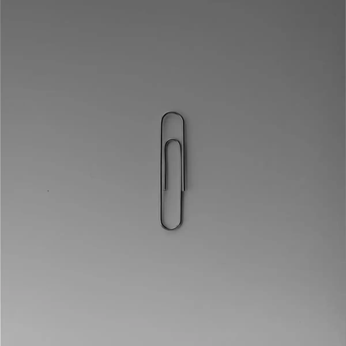 Minimal black-and-white image of a single paperclip centred on a neutral background, representing simplicity, focus, and restraint.