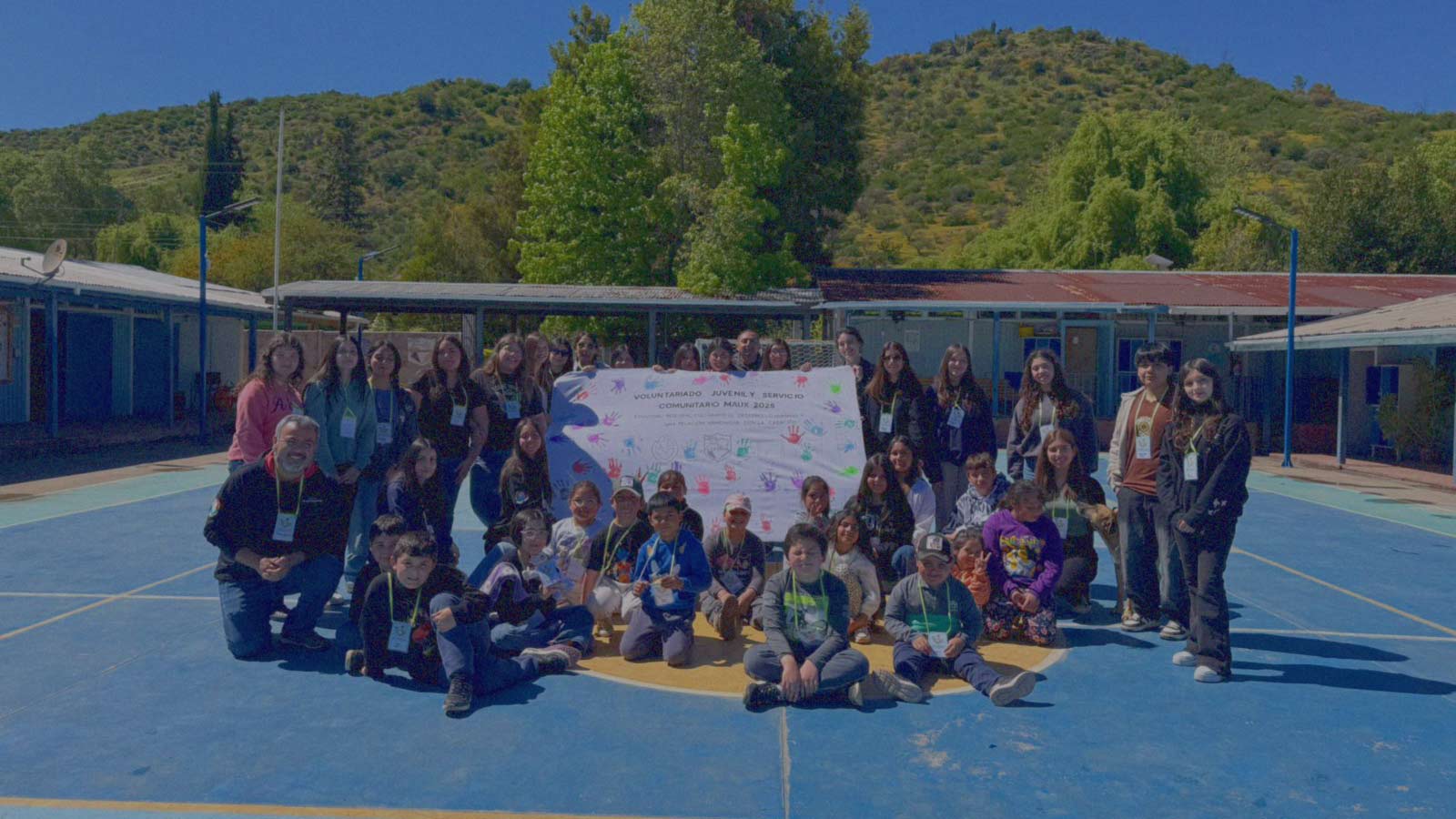 Portada de Servicio x Chile, programa de formación de IdeaPaís, mostrando a escolares que posan junto a niños más pequeños en una cancha deportiva, mientras algunos sostienen una pancarta con manos marcadas con pintura de colores. 