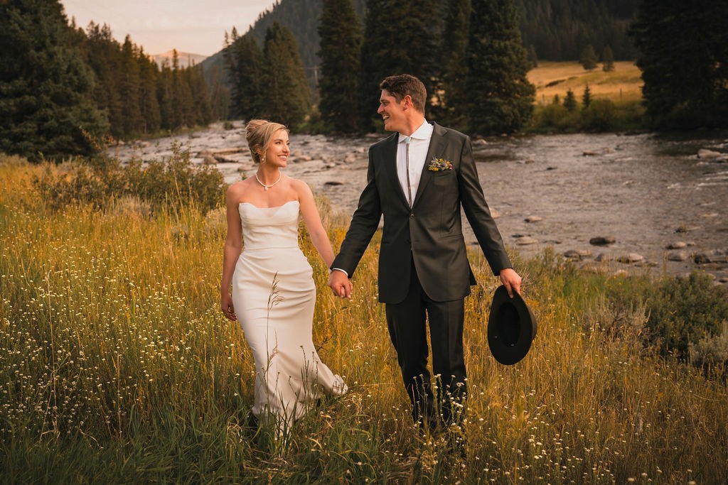 Newlyweds walking through wildflowers beside a river