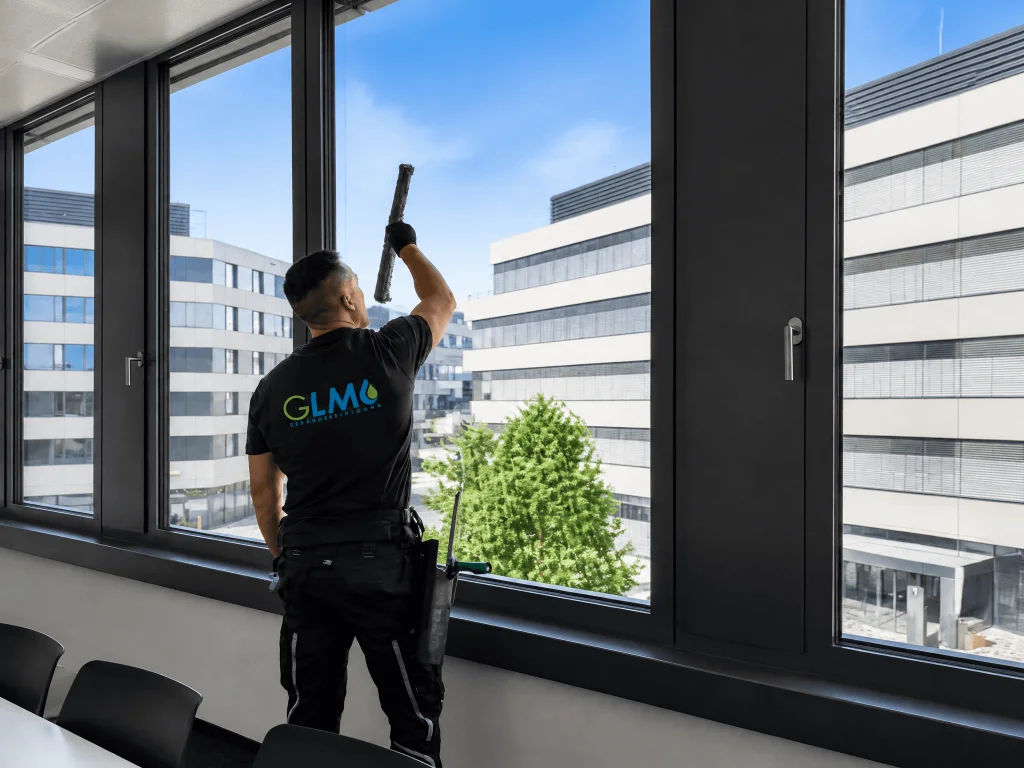 Ein Glasreiniger der GLM Gebäudereinigung von hinten fotografiert, während er mit einem Einwascher eine große Glasfläche reinigt