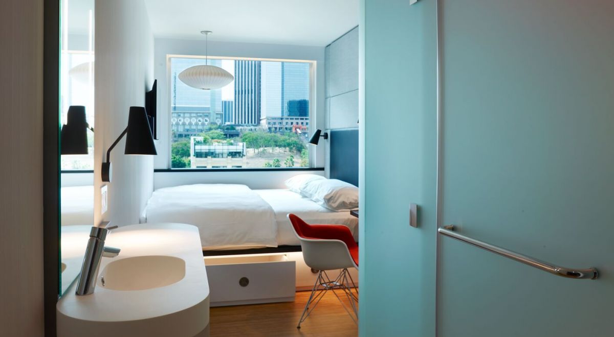 Entry view of a typical guestroom interior, featuring a sleek modern vanity, a large window, and a bed spanning wall to wall.