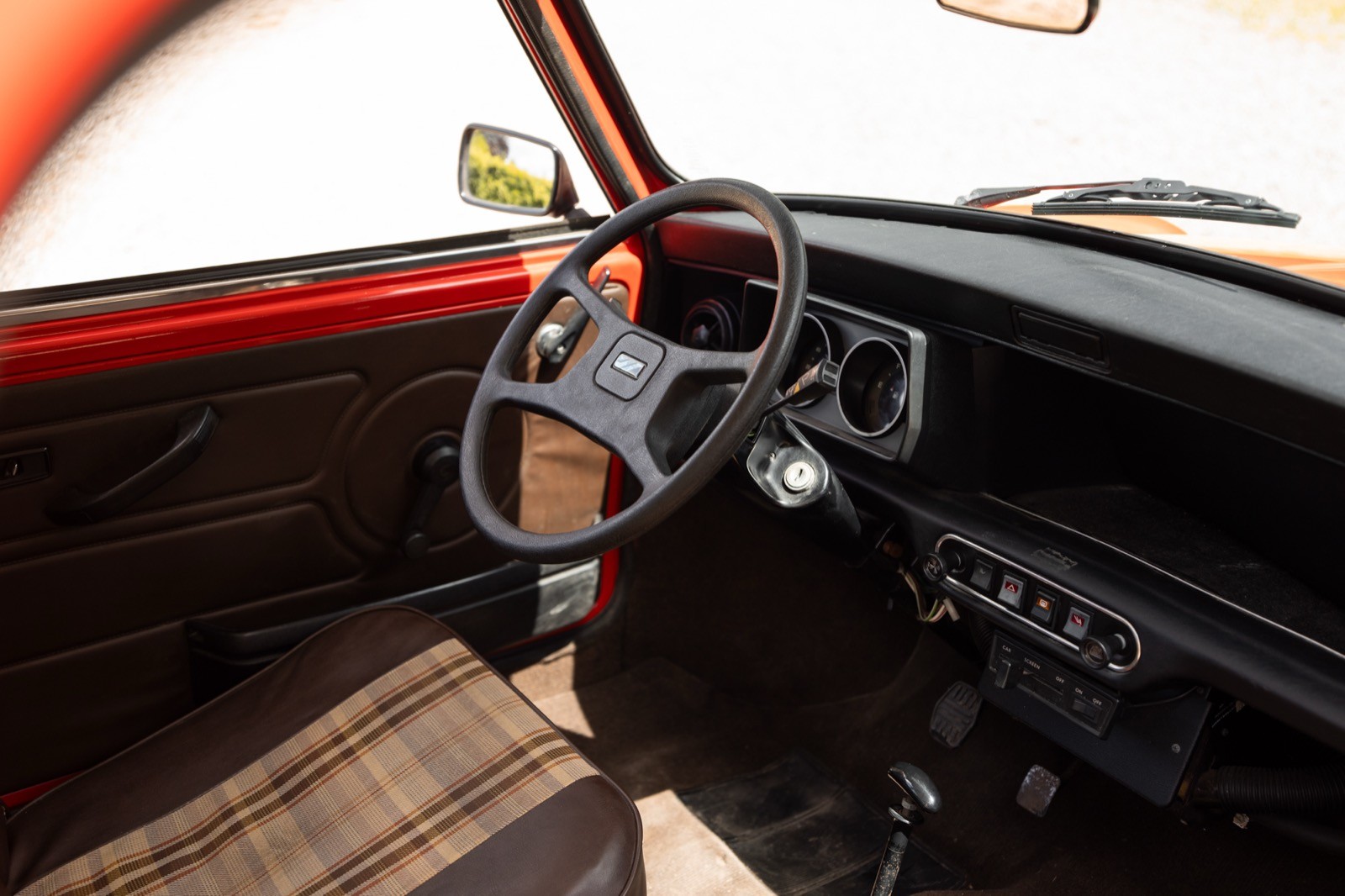 Close-up of a vintage car's interior, featuring a black steering wheel and dashboard with wood accents.