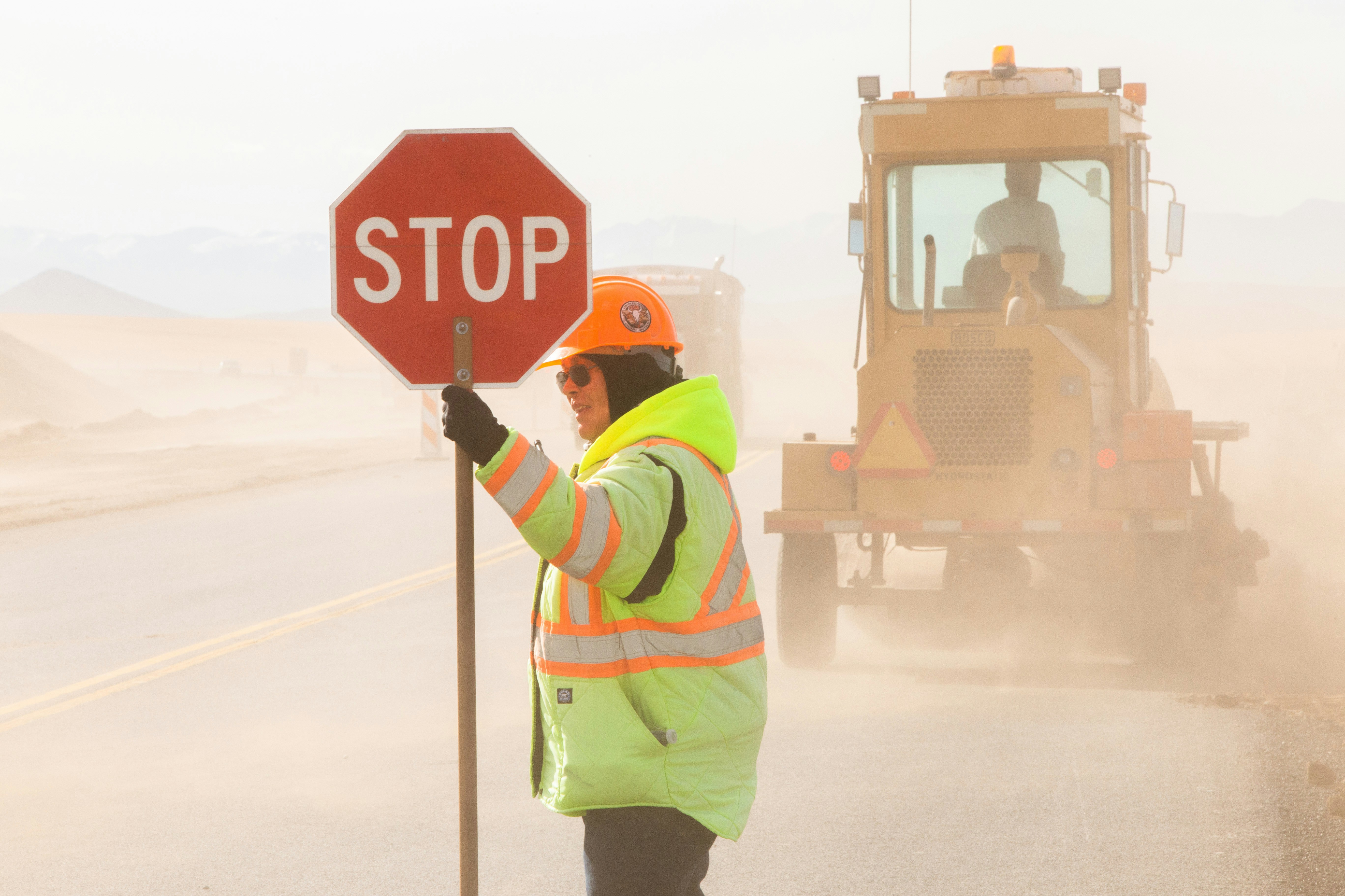 road construction worker holding stop sign with heavy machinery in background