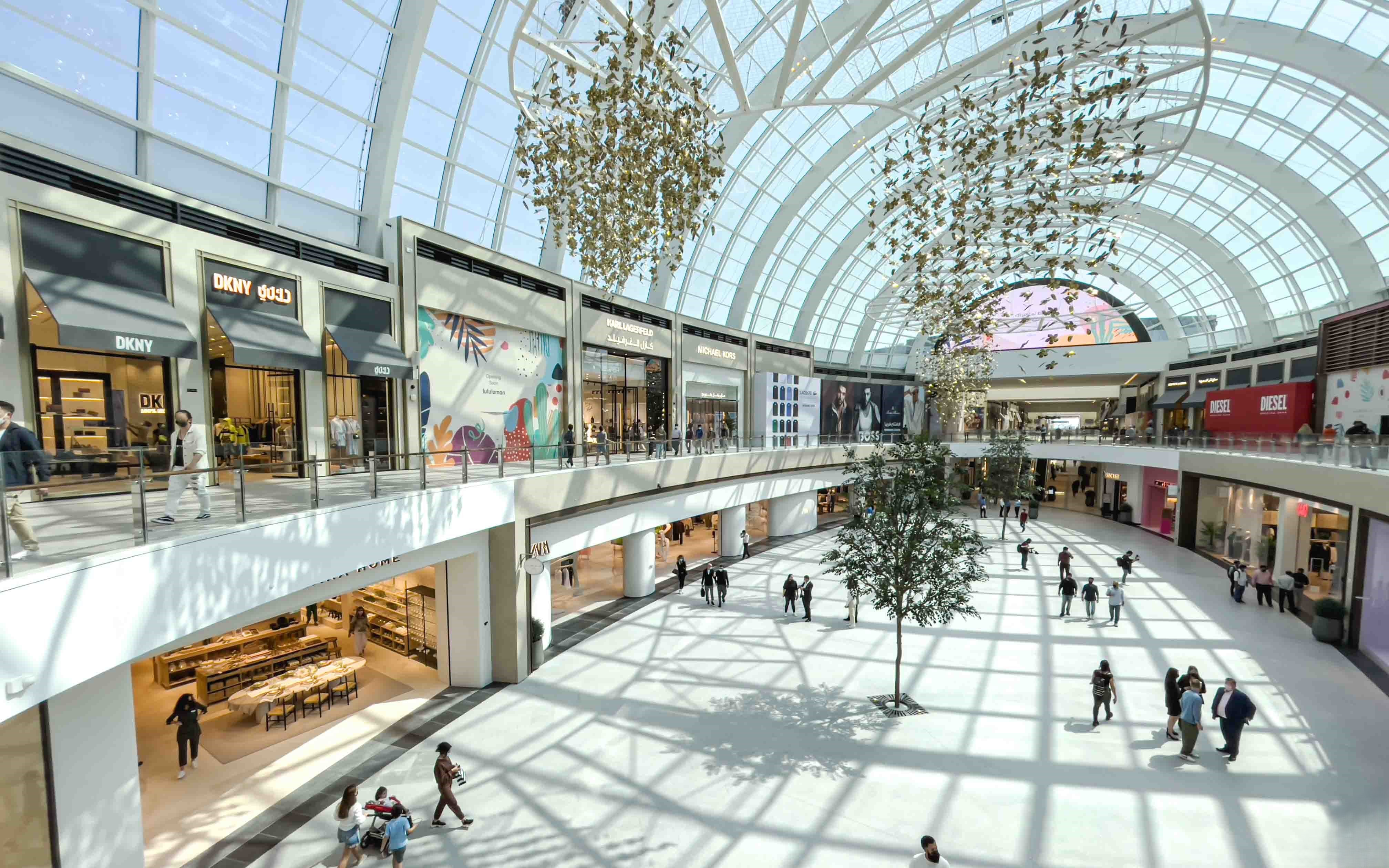 Dubai Hills Estate mall with curved glass ceiling, designer stores, and artistic hanging decor in a bright retail space.