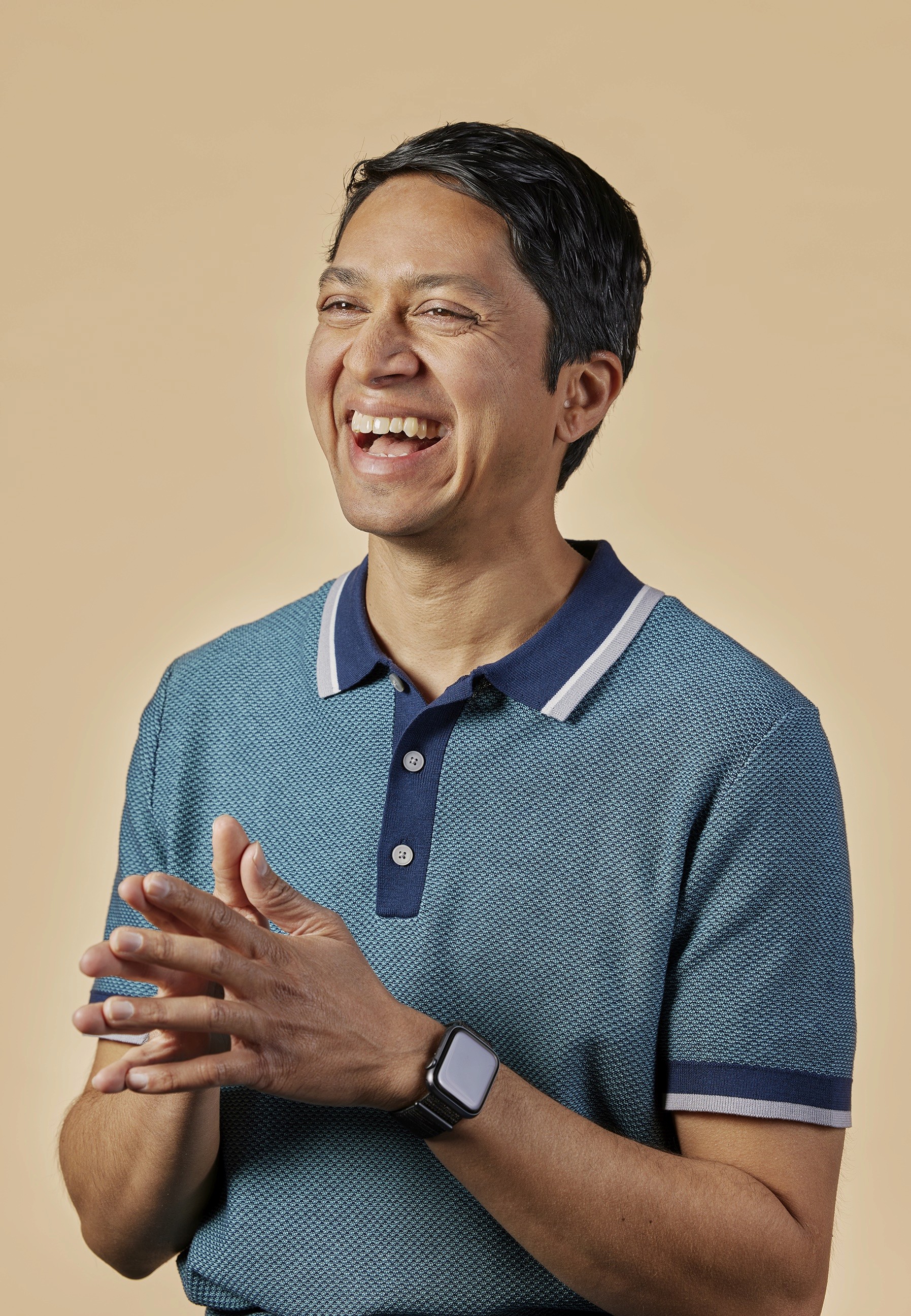 Portrait of man smiling in a blue shirt in front of cream colored backdrop