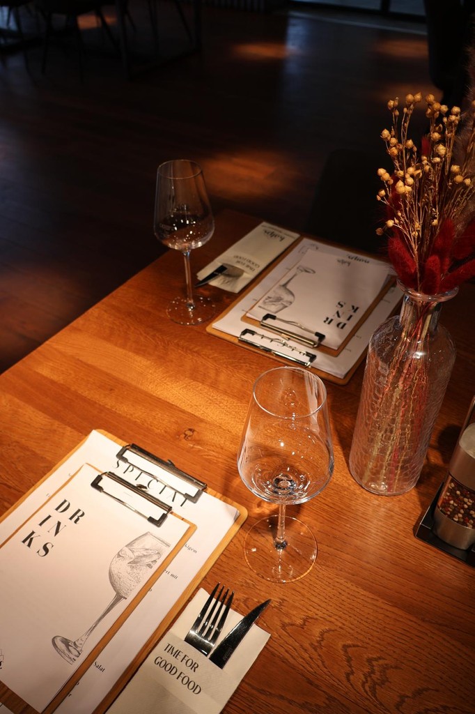 Gedeckter Holztisch im kAlps mit Menükarten, Weingläsern und Trockenblumen in einer Vase.