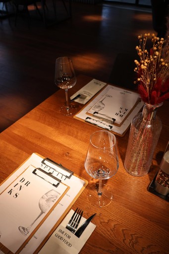 Gedeckter Holztisch im kAlps mit Menükarten, Weingläsern und Trockenblumen in einer Vase.