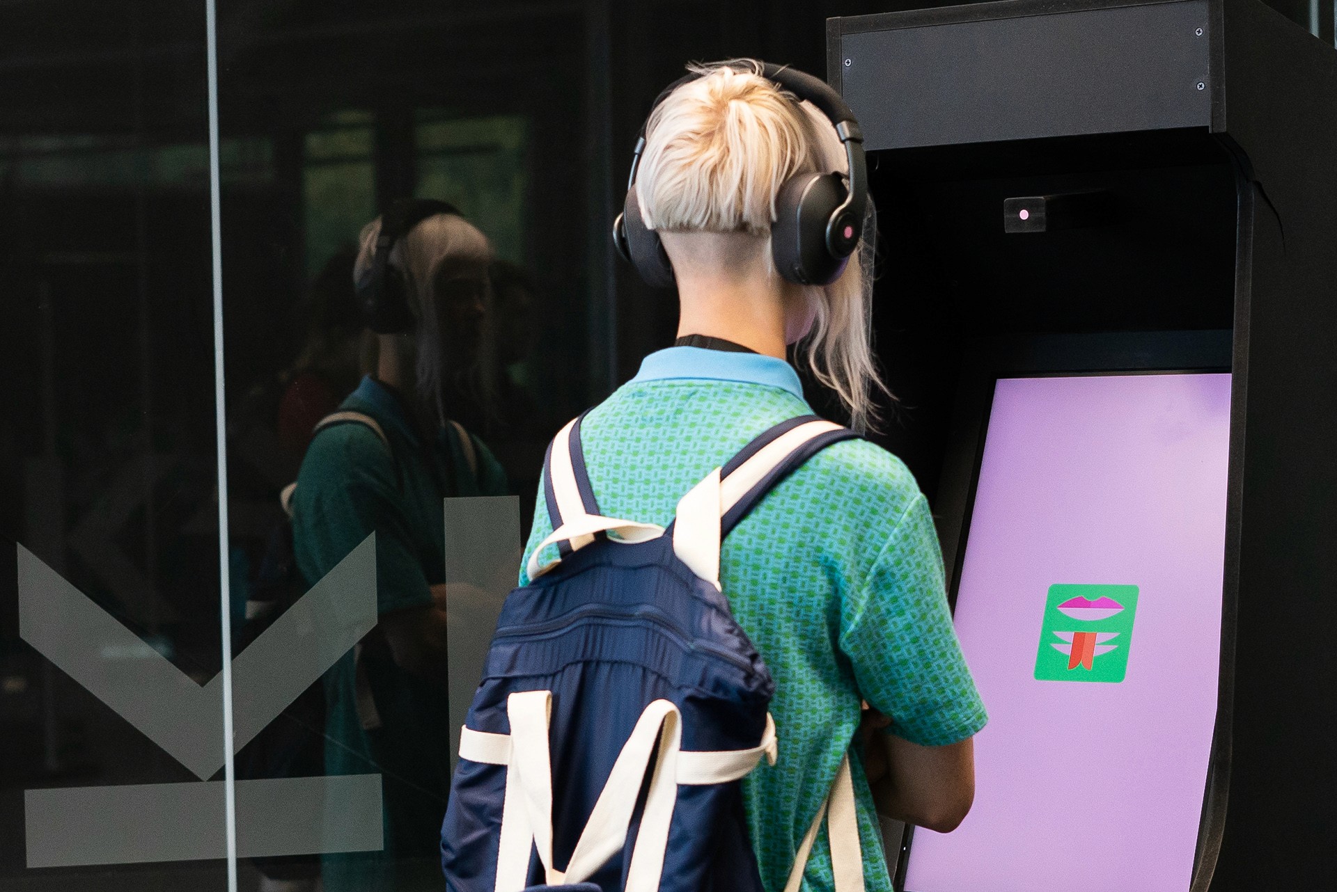 Person with headphones and backpack uses interactive screen.
