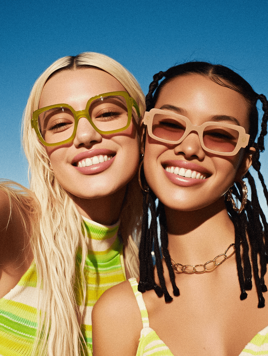 Two women smiling wearing colorful glasses representing beauty and skincare lifestyle.