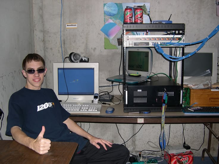A man gives a thumbs up beside an aging server rack, representing used computer parts kept running