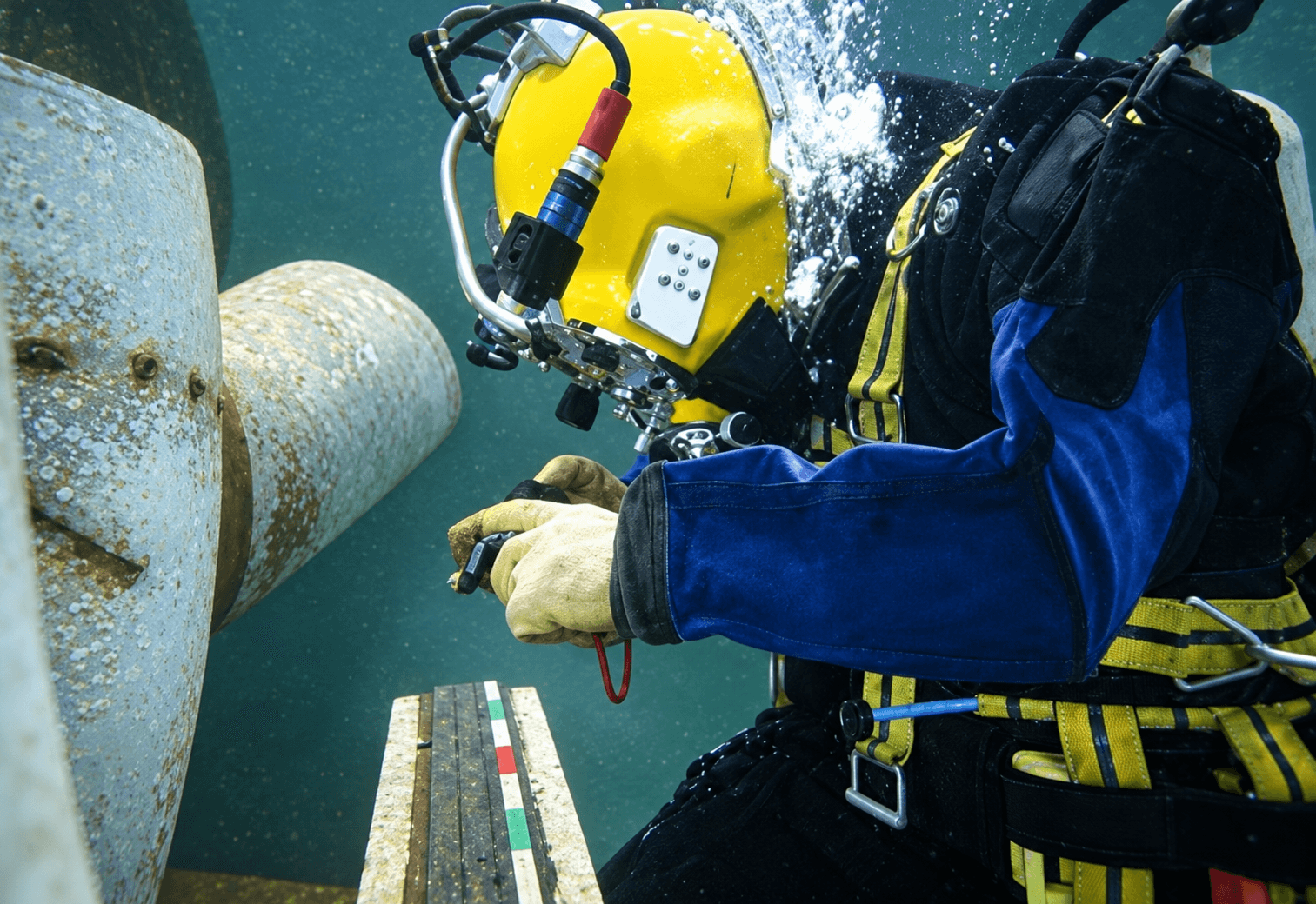 Illustrative underwater examination by a helmeted diver beside a submerged structure.