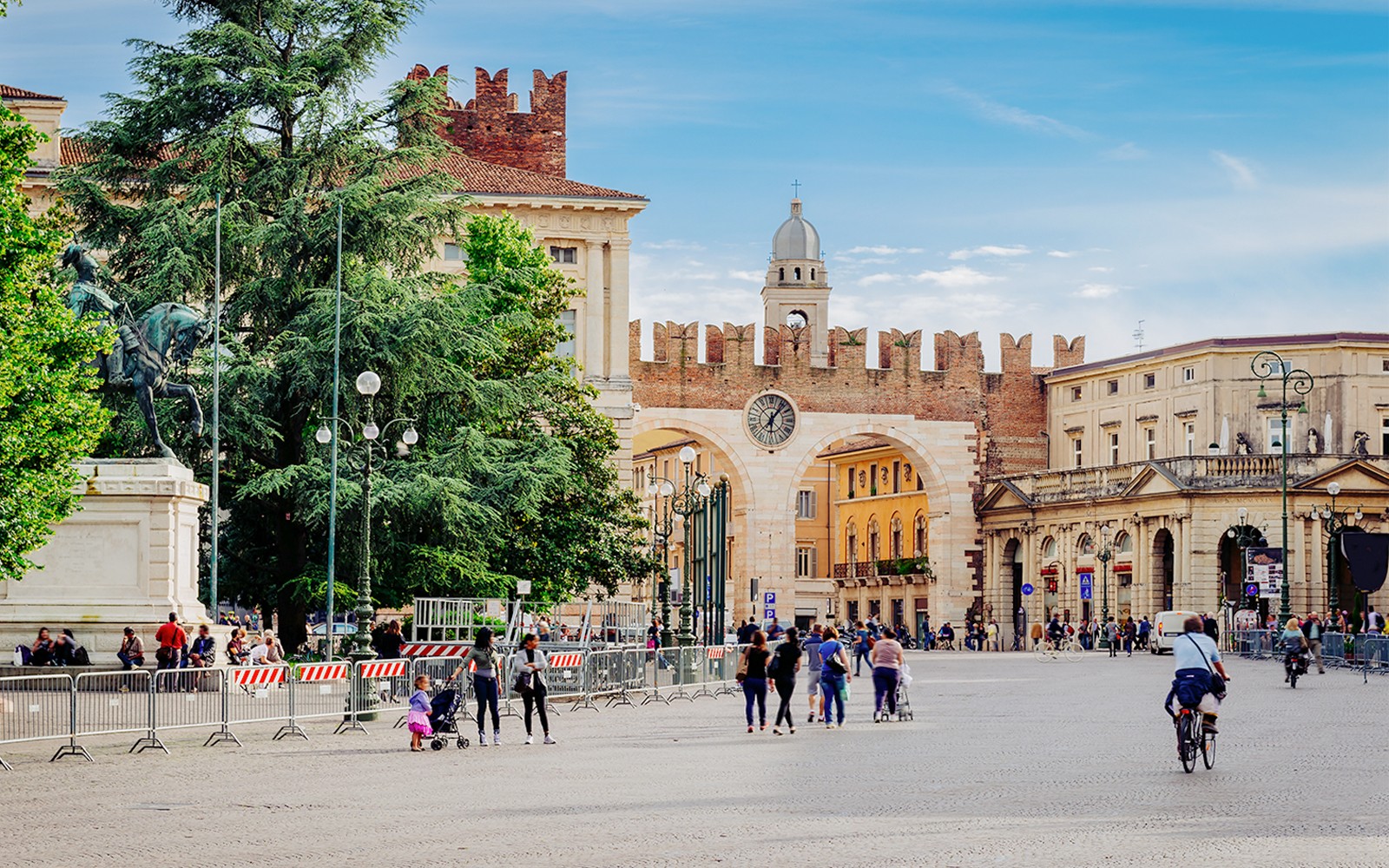 Středověké brány a hodinová věž na náměstí Piazza Bra ve Veroně, Itálie, s lidmi, kteří se procházejí poblíž.