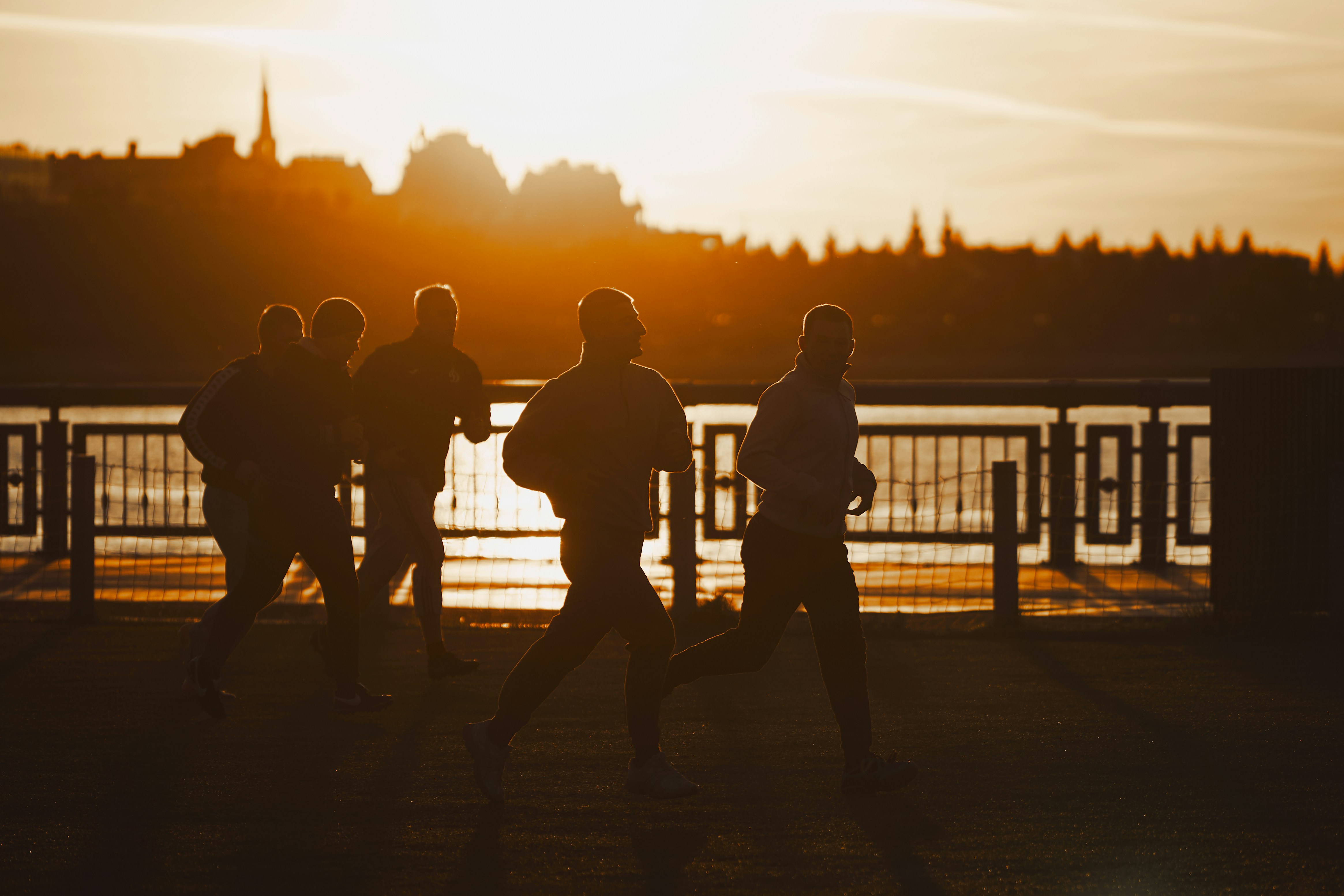 Silhouettes of people running along a waterfront at sunset.