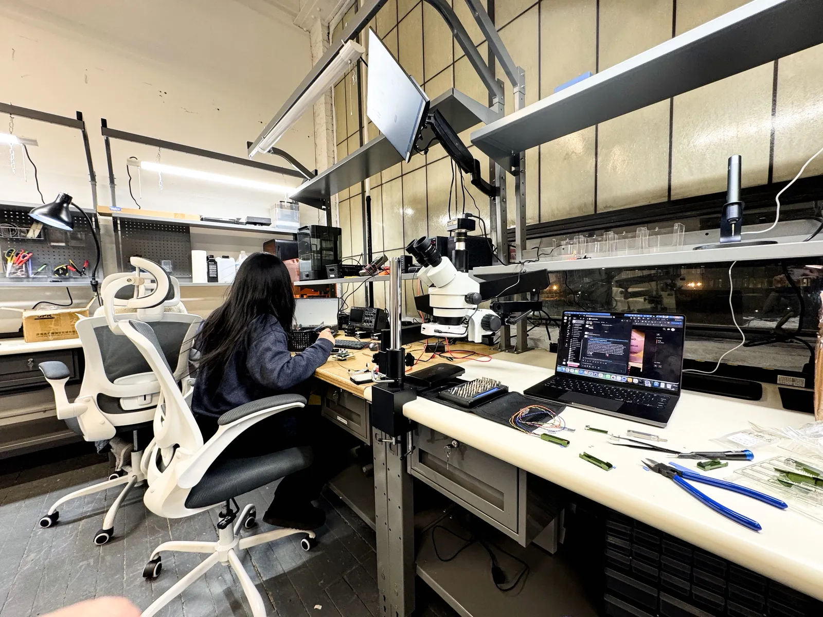 Engineer working at an electronics workbench with a microscope in the BotBlox lab