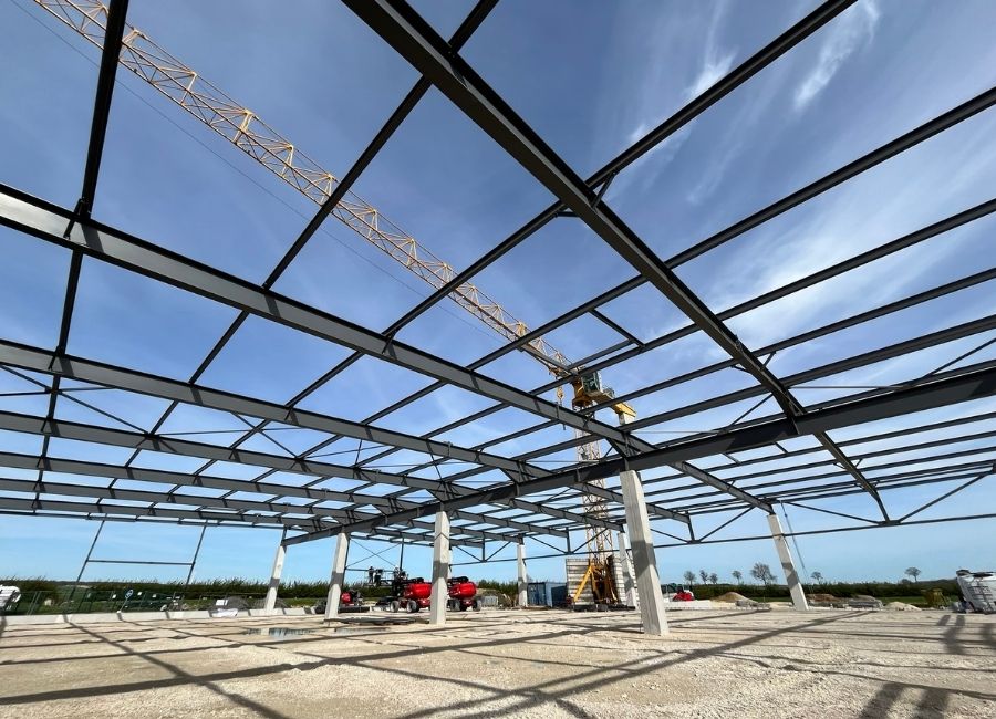 Structure métallique en cours d’assemblage sur chantier, sous un ciel bleu partiellement nuageux.