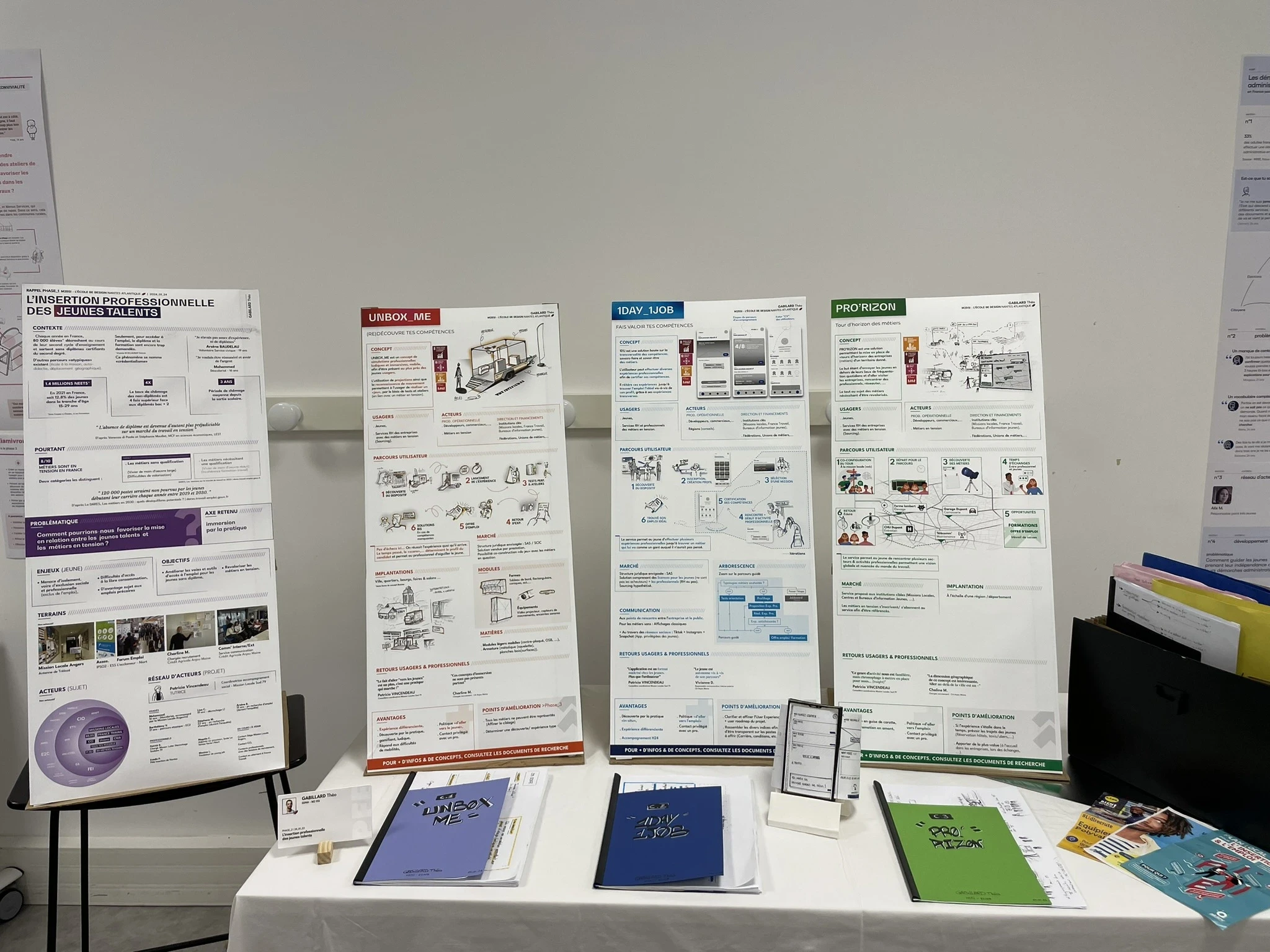 Photographie d'un stand présentant trois concepts. Le stand est composé de quatres panneaux verticaux posés sur une table. Sur cette table est aussi déposé différents dossiers qui font références aux panneaux situés derrière.