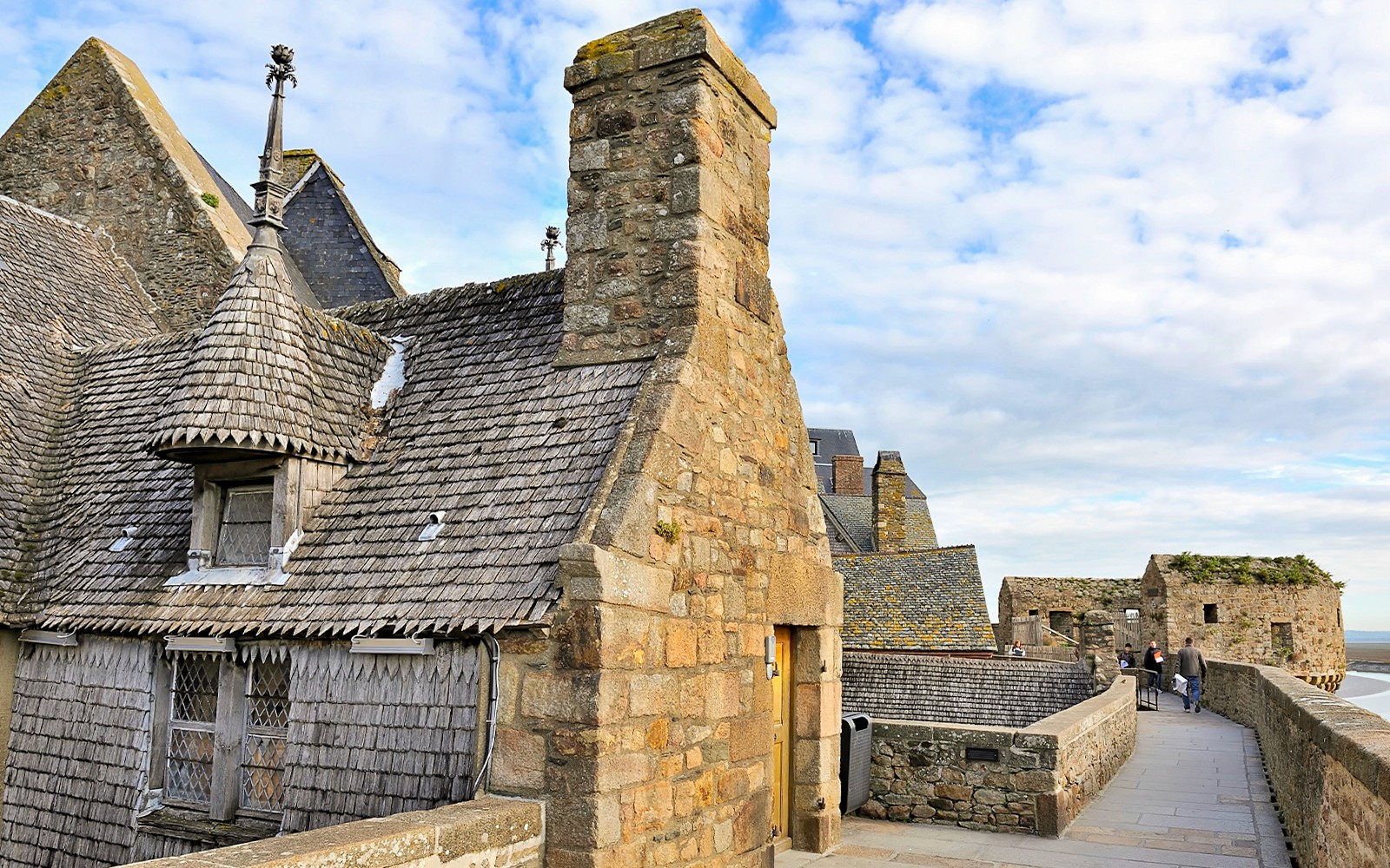 Remparts of Mont Saint Michel with stone buildings and walkway under a blue sky.