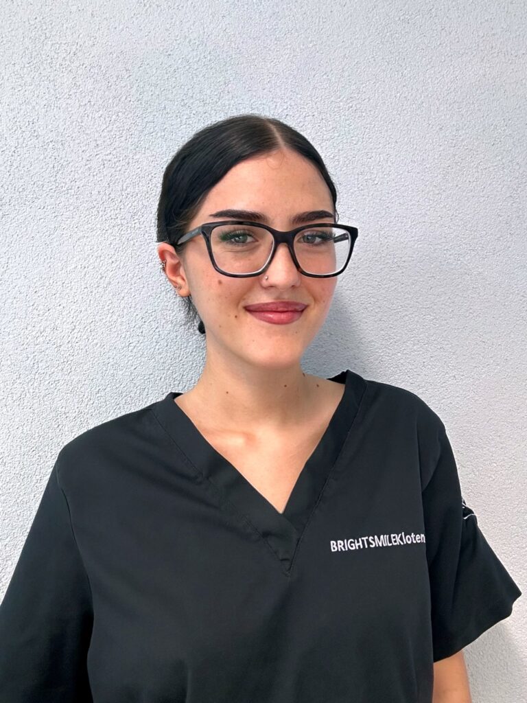 Dentalassistentin Doresa Hasani im Portrait mit schwarzem Zopf und einer Brille. 