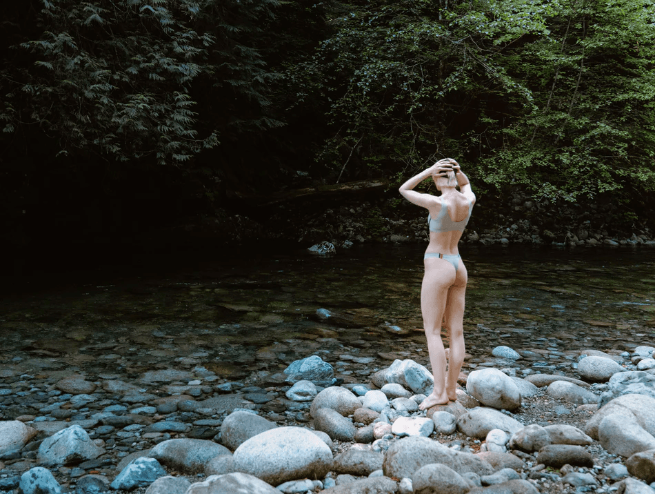 Athlete standing on riverside rocks wearing Surface Athletics performance swimwear designed for freedom of movement and high-performance in and out of the water.